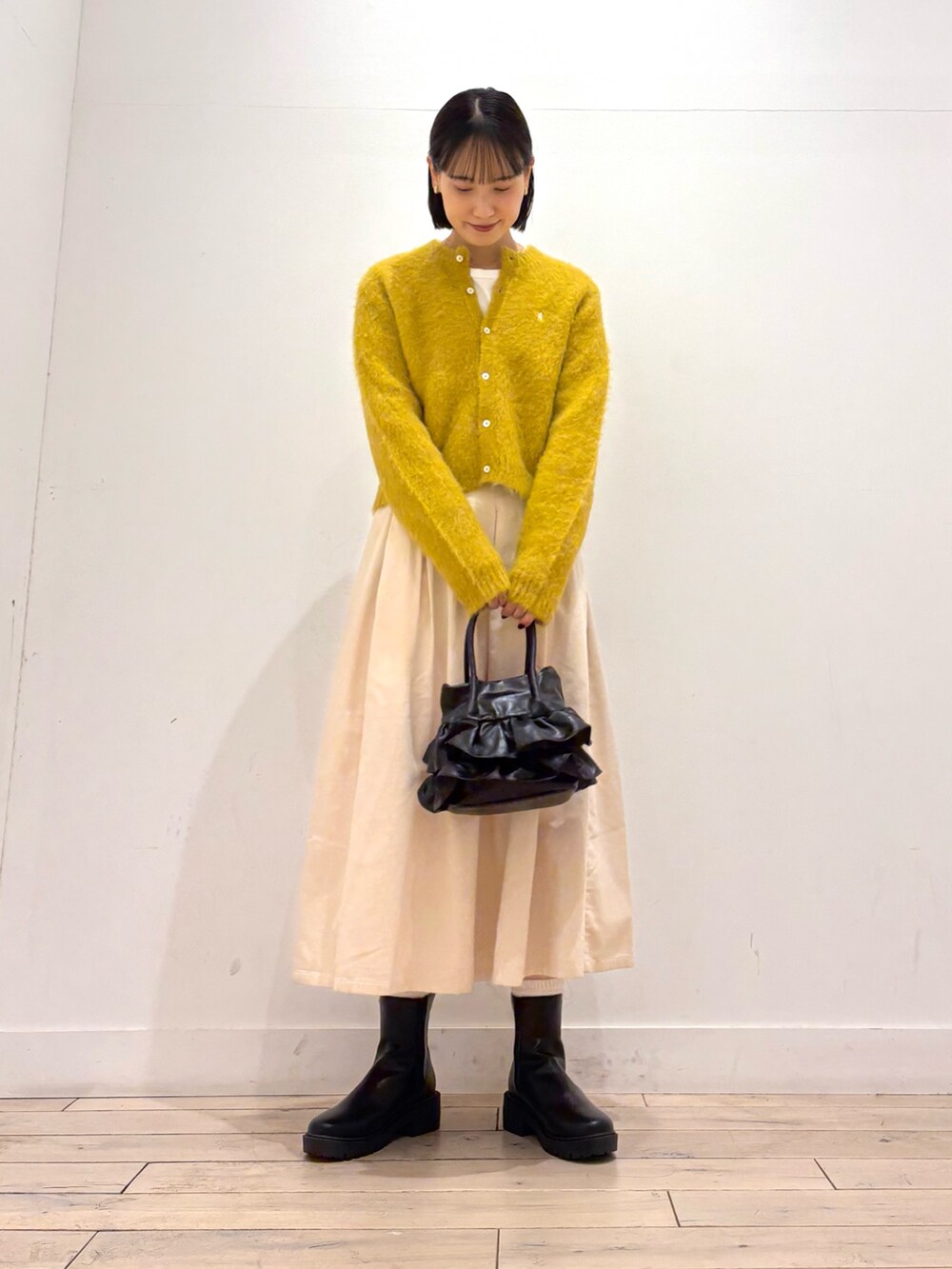 イエロー系のカーディガン/ボレロ、ブラック系のブーツ、ホワイト系のスカートを着用したレディースの秋コーディネートの3枚目の写真