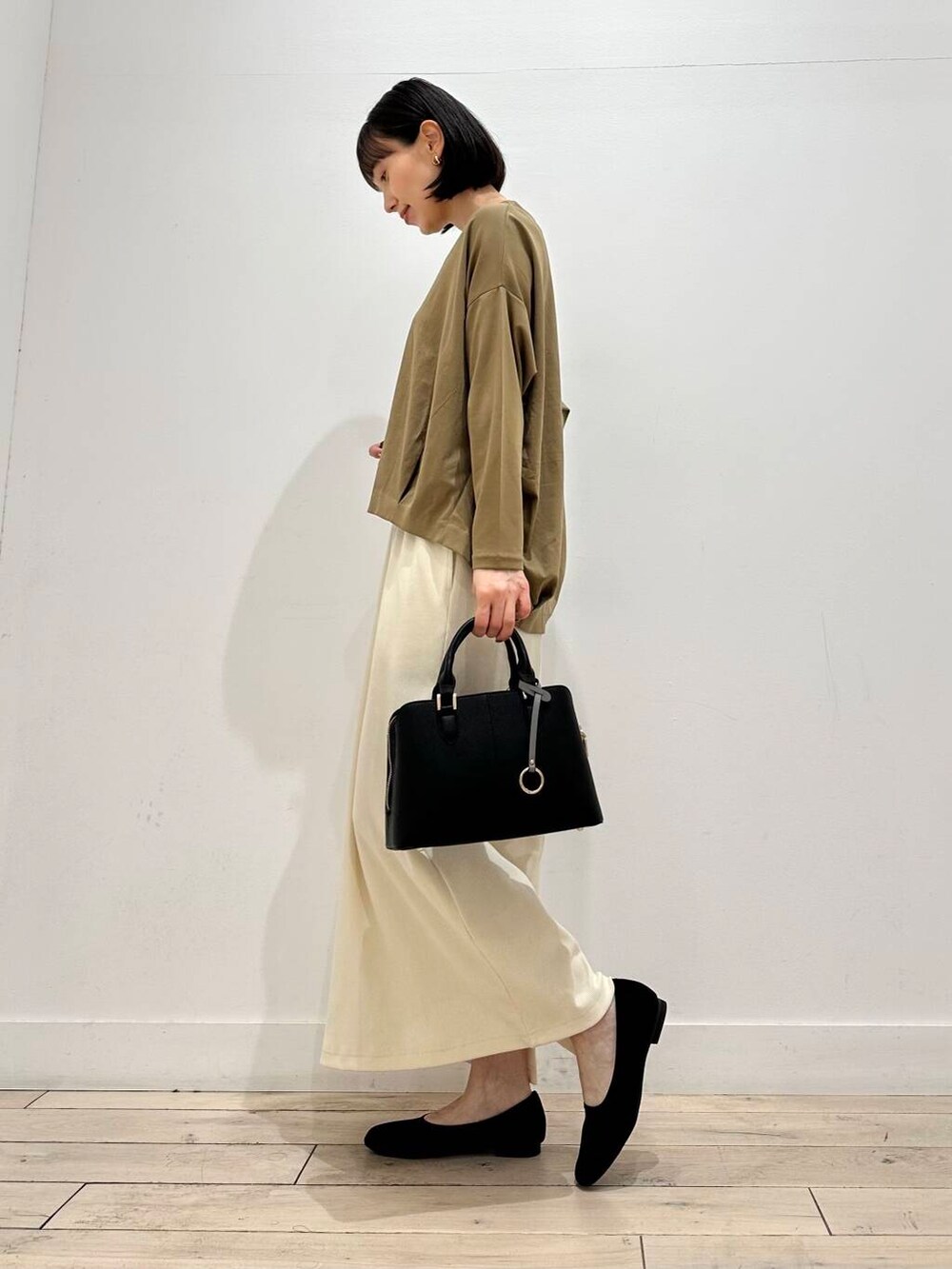 ホワイト系のスカート、ベージュ系のTシャツ/カットソー、ブラック系のハンドバッグを着用したレディースの秋コーディネートの2枚目の写真