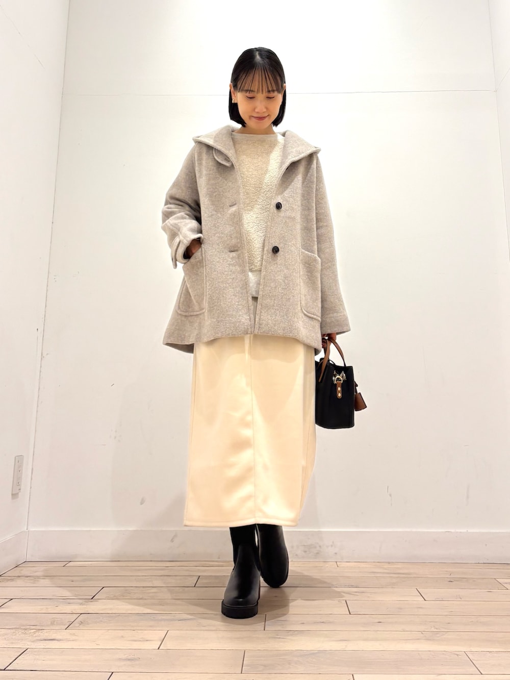 ブラック系のブーツ、ブラック系のハンドバッグ、ホワイト系のスカートを着用したレディースの冬コーディネートの2枚目の写真