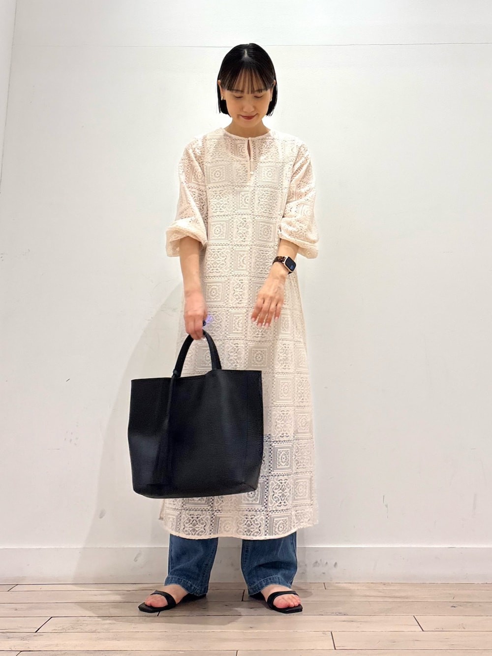 ベージュ系のワンピース、ブルー系のデニムパンツ、ブラック系のトートバッグを着用したレディースの春コーディネートの2枚目の写真