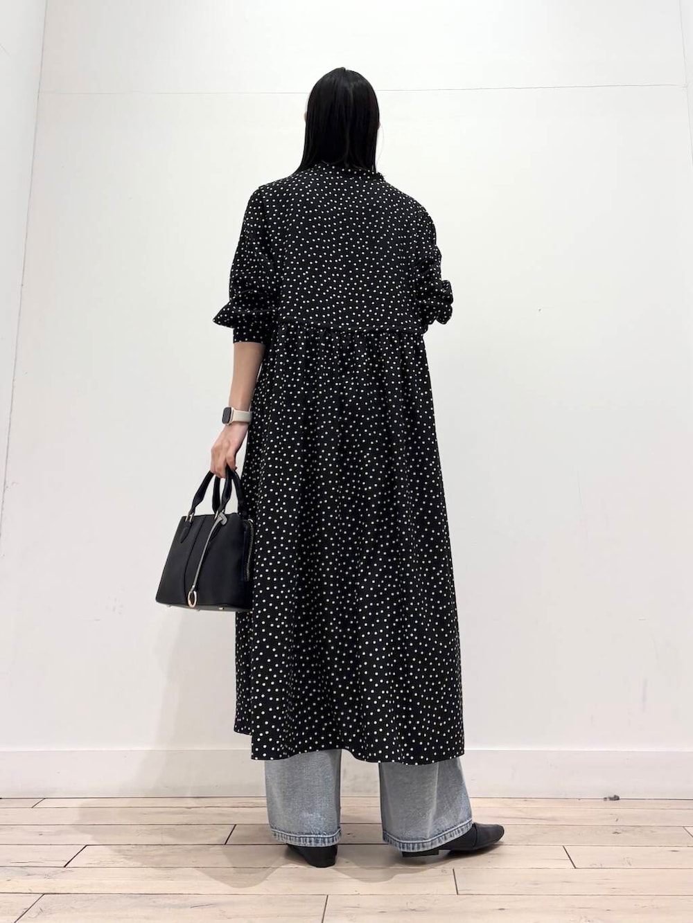 ブラック系のハンドバッグ、ブルー系のデニムパンツ、ブラック系のワンピースを着用したレディースの春コーディネートの3枚目の写真