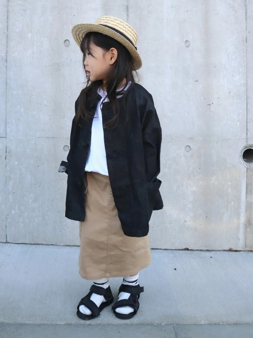 ブラック系のデニムジャケット、ベージュ系のスカート、ブラック系のサンダルを着用したキッズの春コーディネートの3枚目の写真