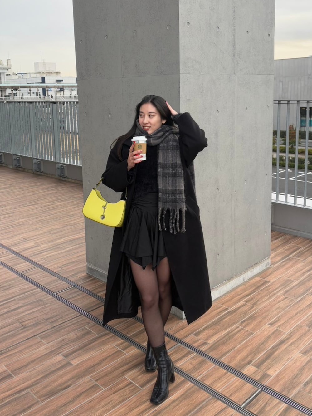 イエロー系のハンドバッグ、ブラック系のスカート、ブラック系のチェスターコートを着用したレディースの冬コーディネートの2枚目の写真