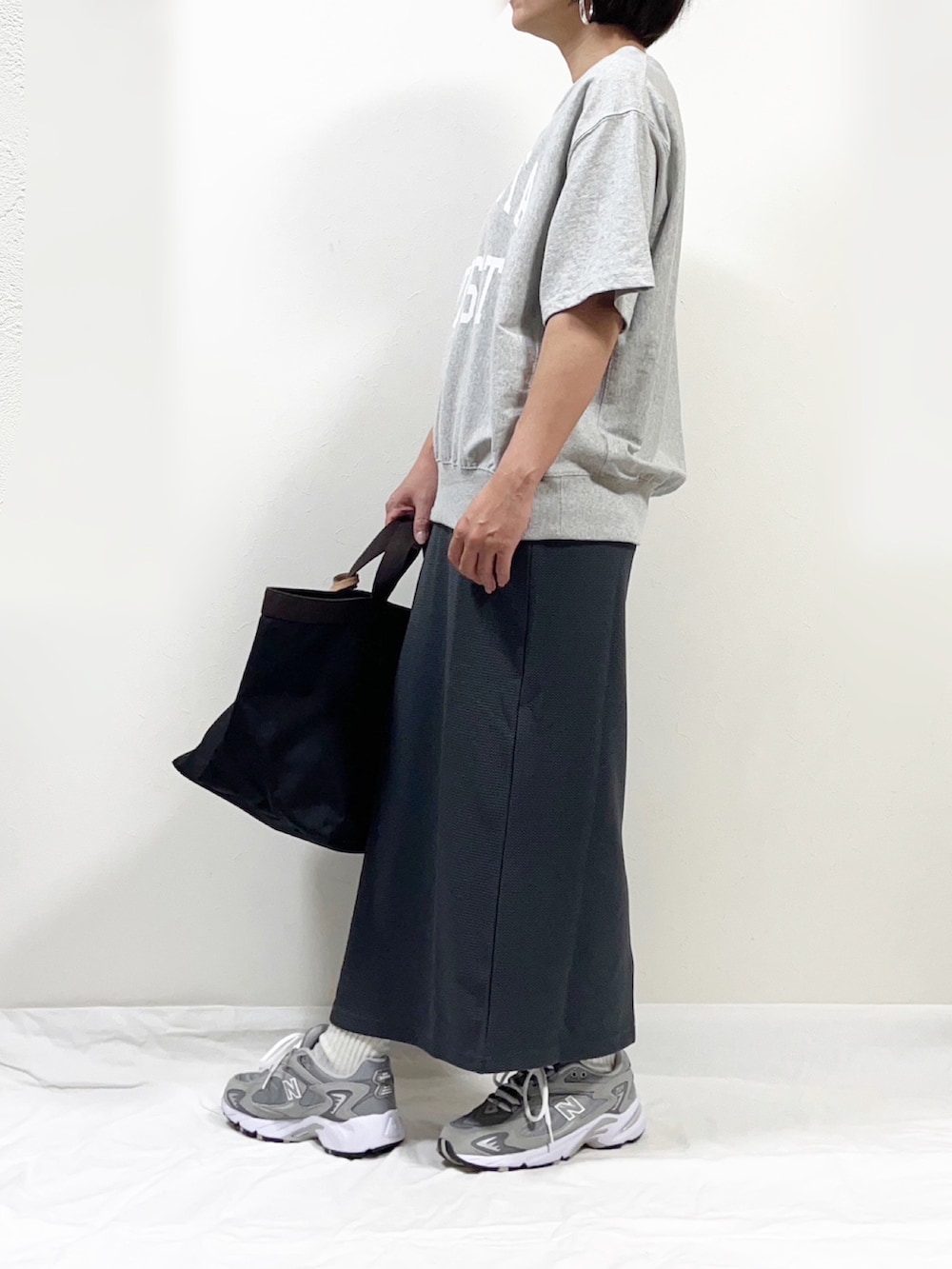グレー系のスカート、グレー系のスニーカー、ブラック系のトートバッグを着用したレディースの秋コーディネートの2枚目の写真