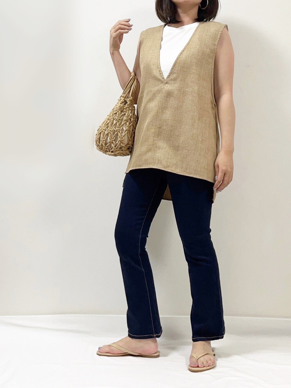 ベージュ系のベスト、ブルー系のデニムパンツ、ベージュ系のサンダルを着用したレディースの夏コーディネートの2枚目の写真
