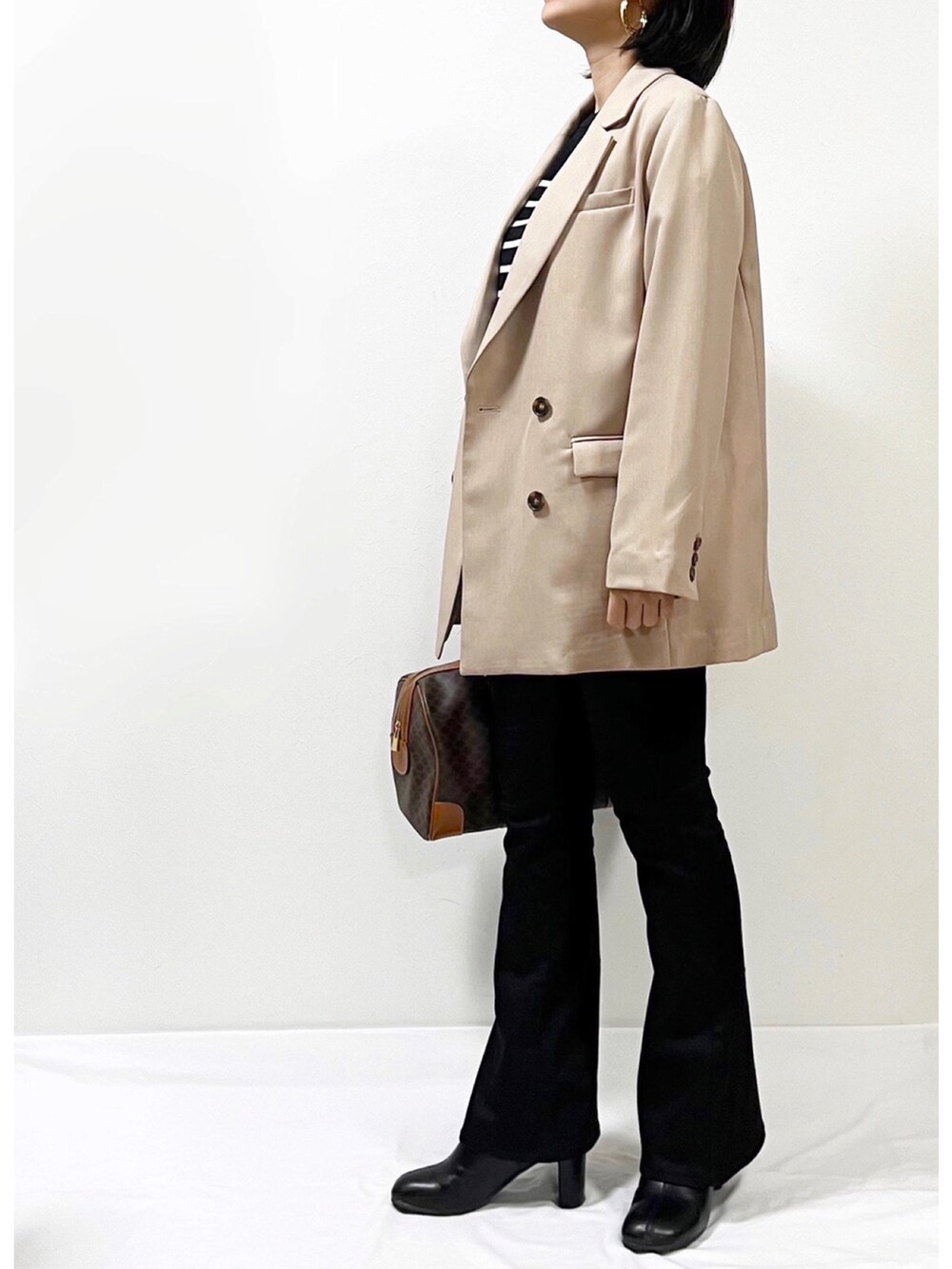 ブラック系のニット/セーター、ベージュ系のテーラードジャケット、ブラック系のデニムパンツを着用したレディースの春コーディネートの2枚目の写真