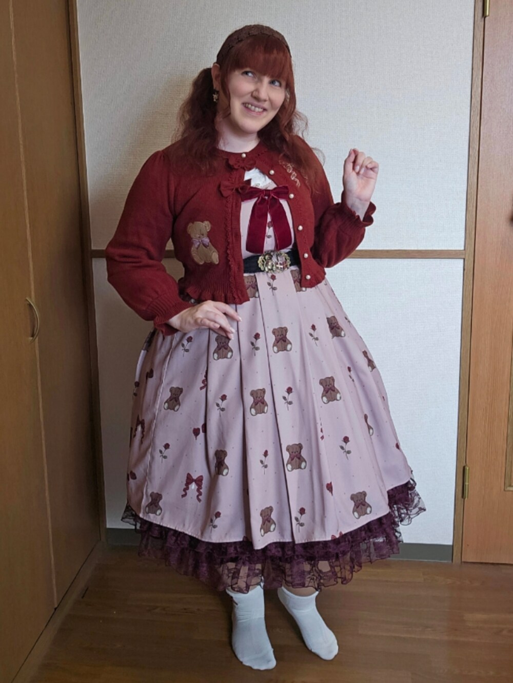 ブラウン系のトートバッグ、ブラウン系のジャンパースカート、レッド系のカーディガン/ボレロを着用したレディースの春コーディネートの2枚目の写真