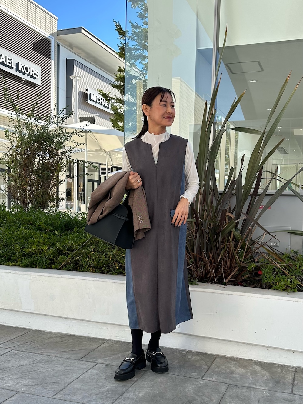 ブラウン系のテーラードジャケット、グレー系のワンピース、ブラック系のトートバッグを着用したレディースの秋コーディネートの6枚目の写真