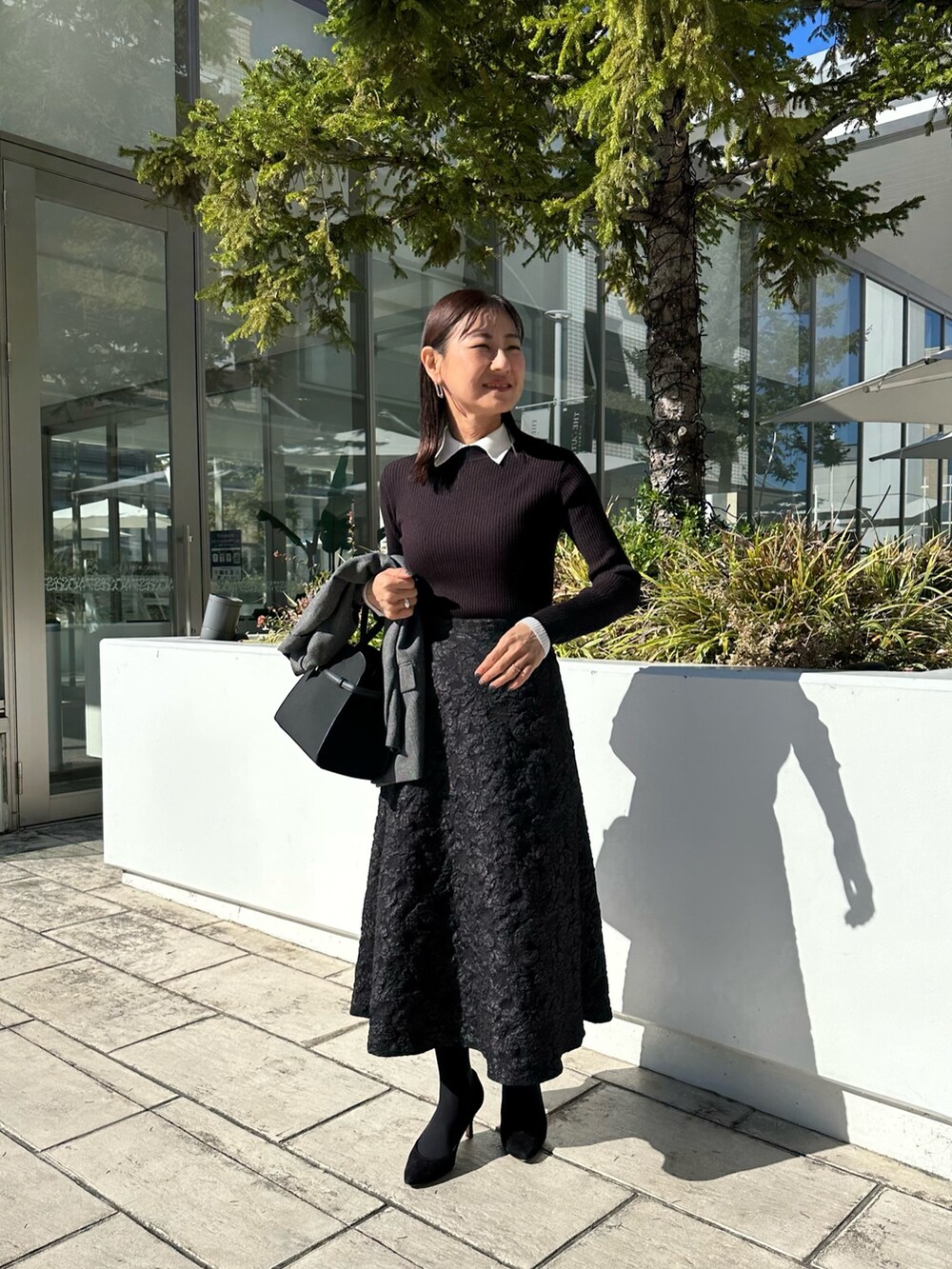 グレー系のテーラードジャケット、ブラック系のニット/セーター、グレー系のスカートを着用したレディースの秋コーディネートの8枚目の写真