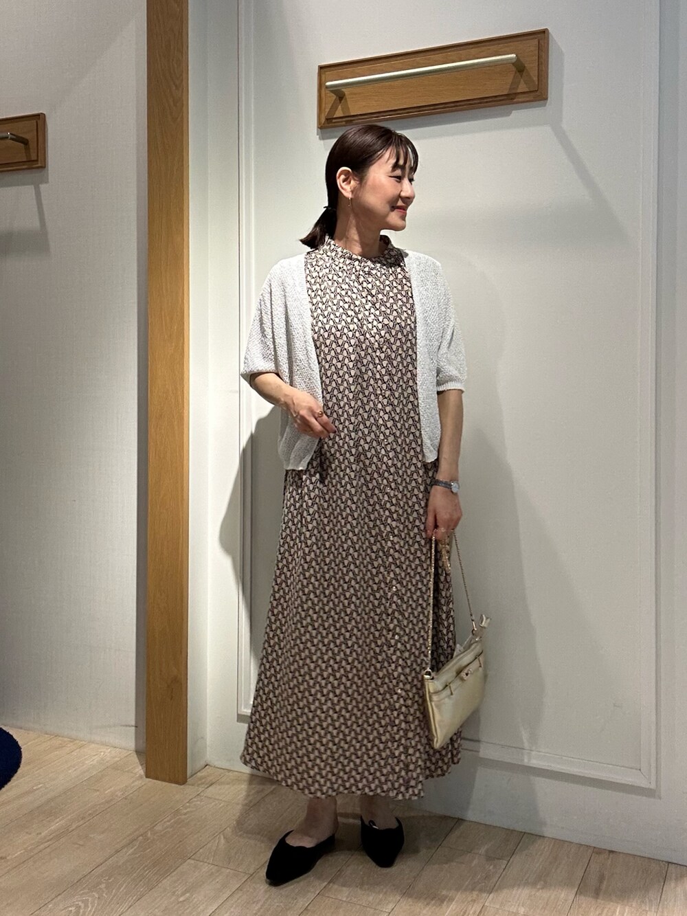 ベージュ系のワンピース、ホワイト系のカーディガン/ボレロ、ゴールド系のショルダーバッグを着用したレディースの春コーディネートの4枚目の写真