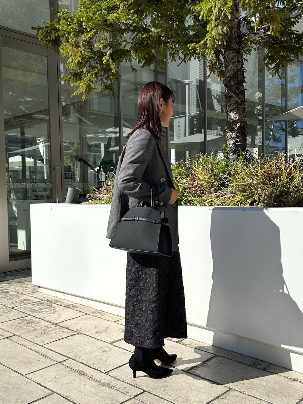 グレー系のテーラードジャケット、ブラック系のニット/セーター、グレー系のスカートを着用したレディースの秋コーディネートの4枚目の写真