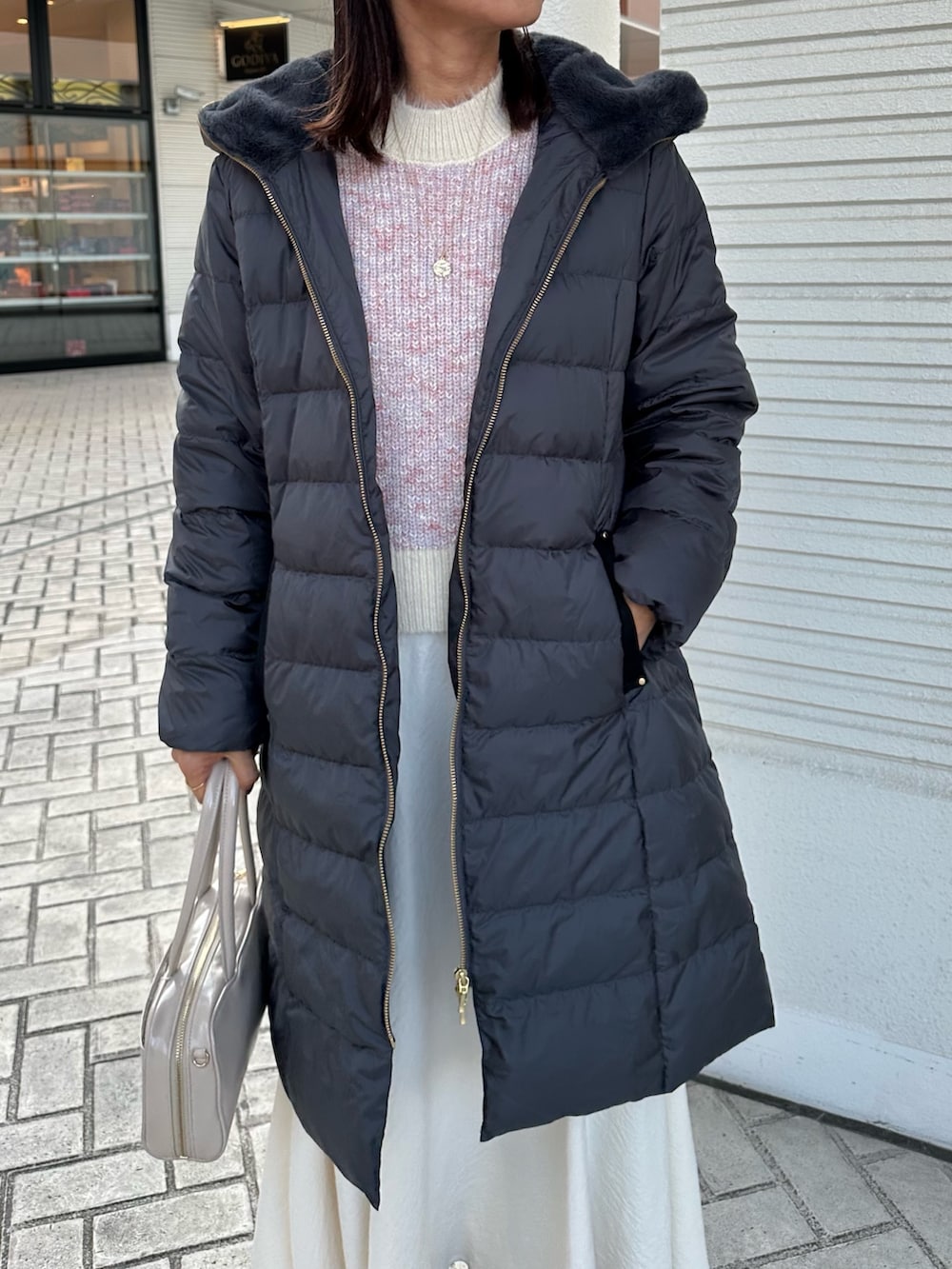 ピンク系のニット/セーター、グレー系のダウンジャケット/コート、ホワイト系のスカートを着用したレディースの冬コーディネートの4枚目の写真