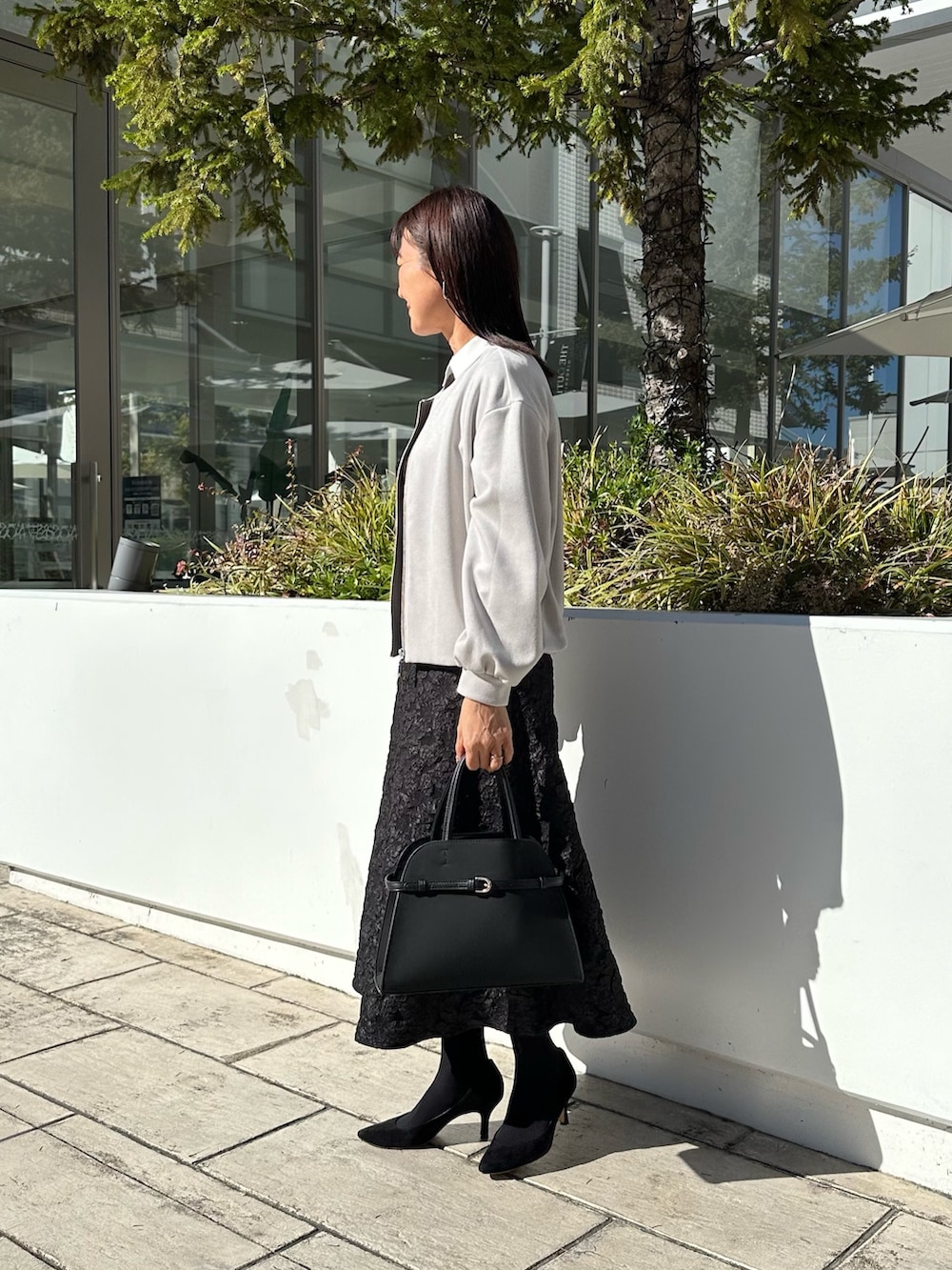 グレー系のブルゾン、ブラック系のニット/セーター、グレー系のスカートを着用したレディースの秋コーディネートの2枚目の写真