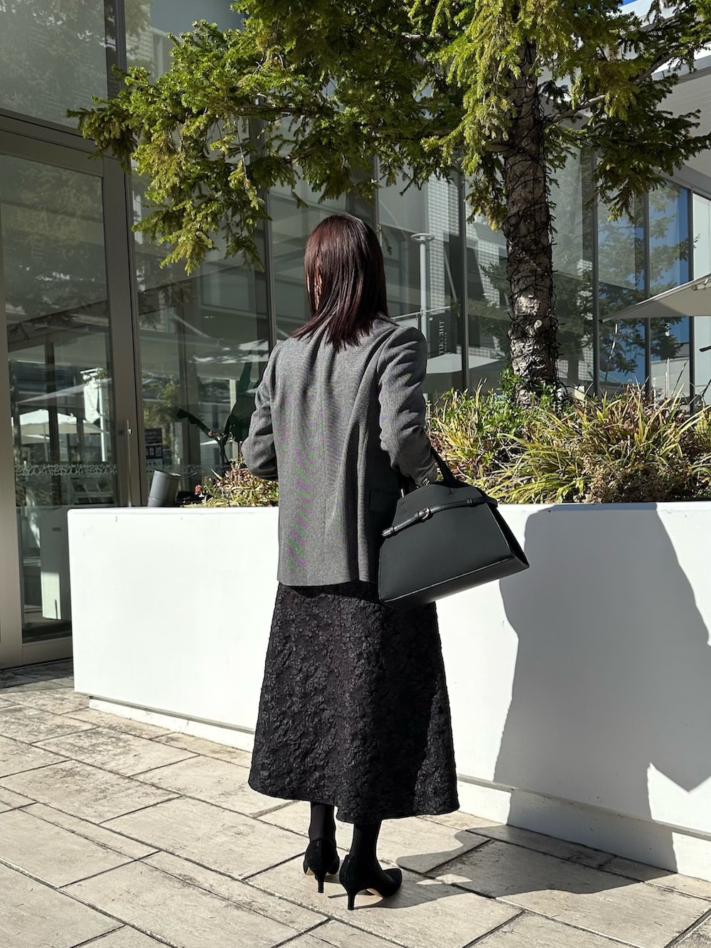 グレー系のテーラードジャケット、ブラック系のニット/セーター、グレー系のスカートを着用したレディースの秋コーディネートの3枚目の写真