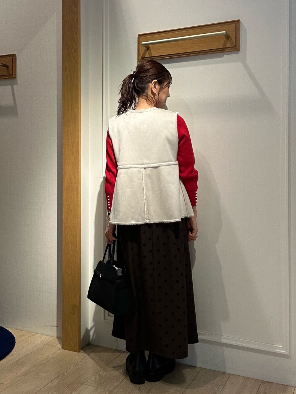 レッド系のニット/セーター、ブラウン系のスカート、ブラック系のトートバッグを着用したレディースの秋コーディネートの7枚目の写真