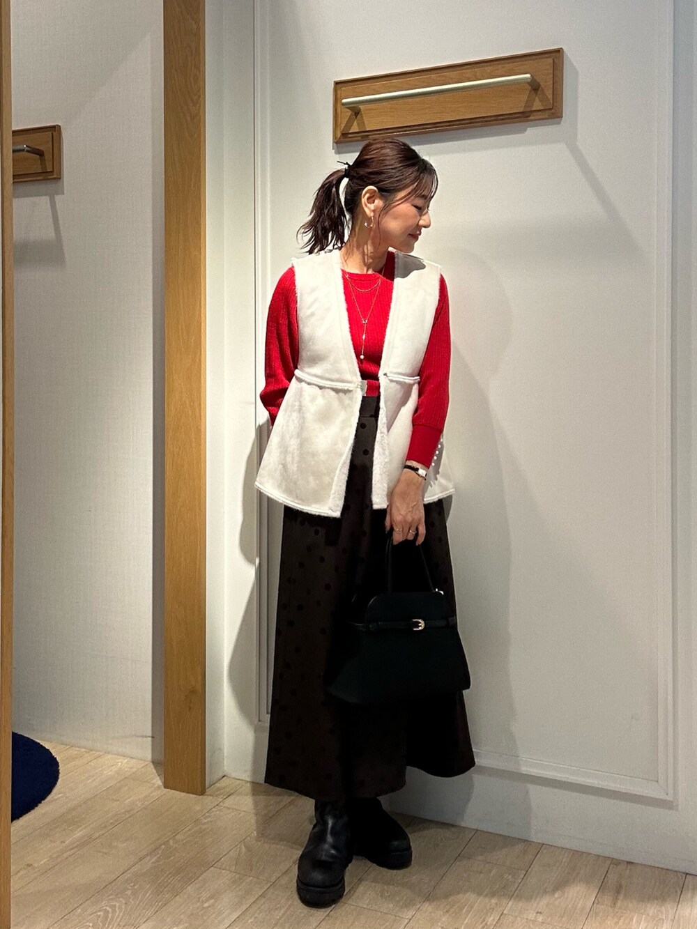 レッド系のニット/セーター、ブラウン系のスカート、ブラック系のトートバッグを着用したレディースの秋コーディネートの6枚目の写真