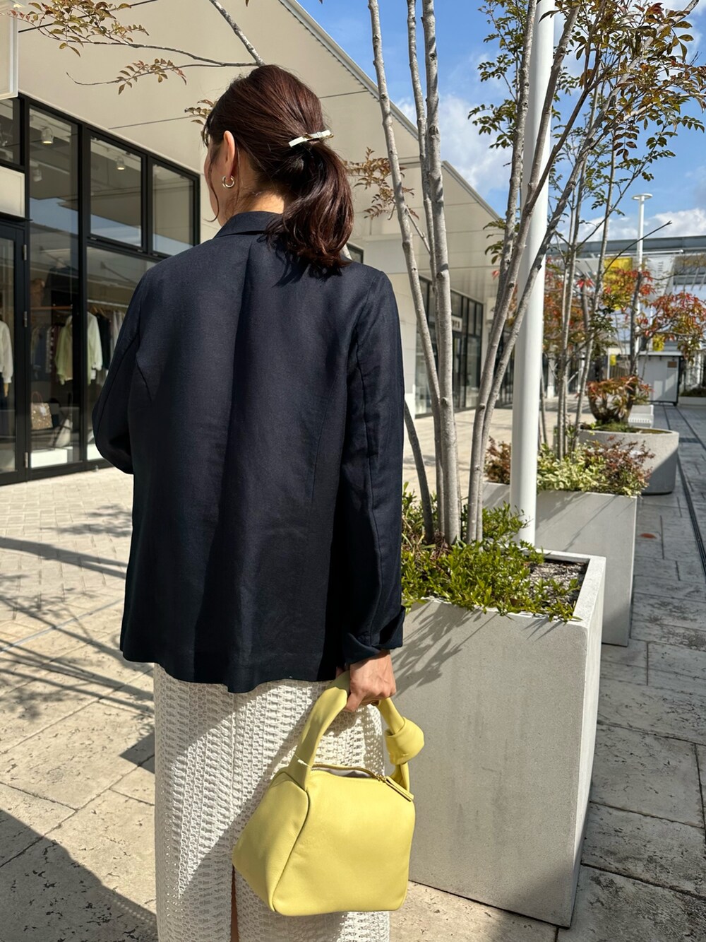 ブルー系のテーラードジャケット、ホワイト系のスカート、イエロー系のショルダーバッグを着用したレディースの春コーディネートの7枚目の写真