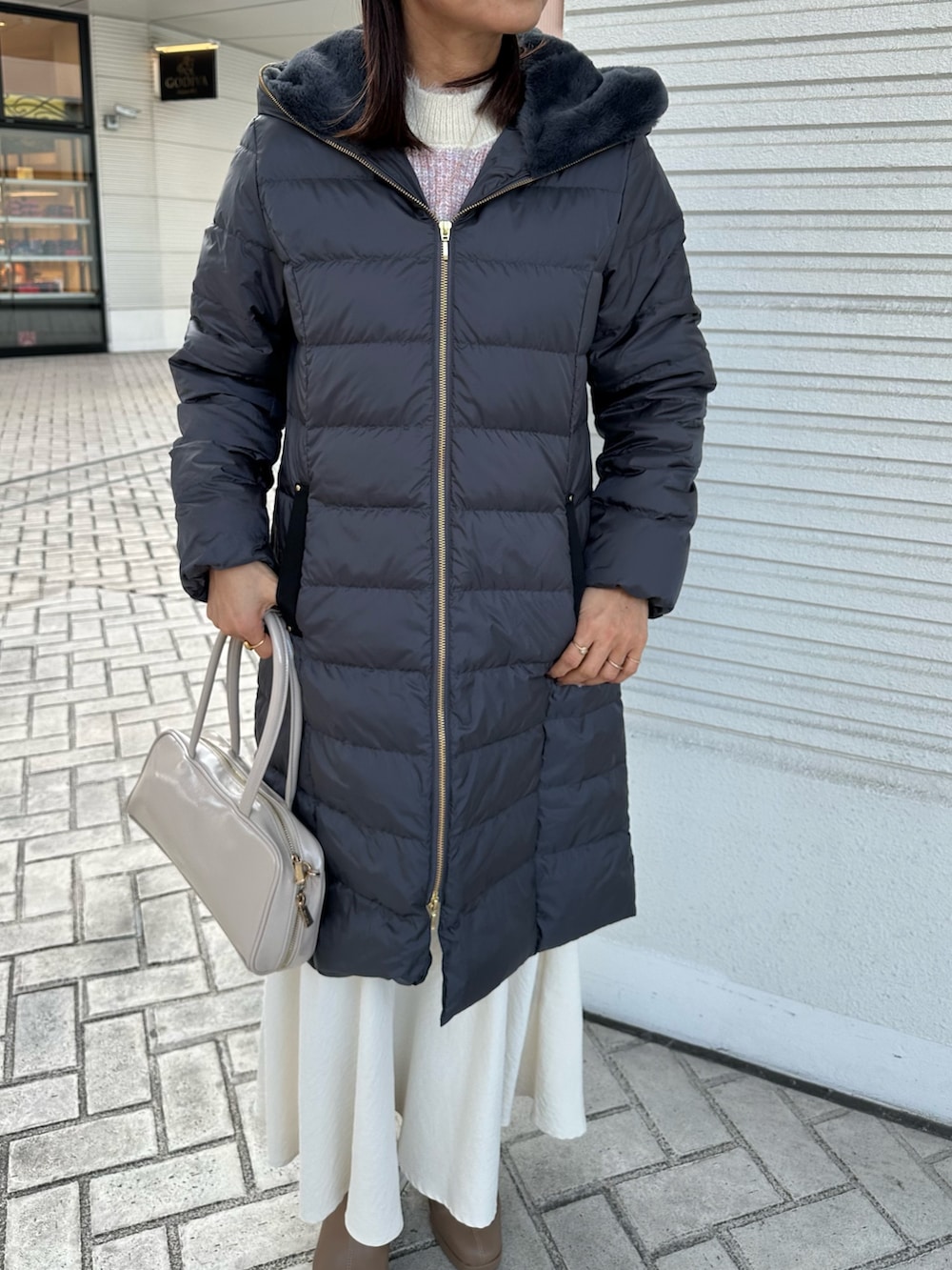 ピンク系のニット/セーター、グレー系のダウンジャケット/コート、ホワイト系のスカートを着用したレディースの冬コーディネートの7枚目の写真