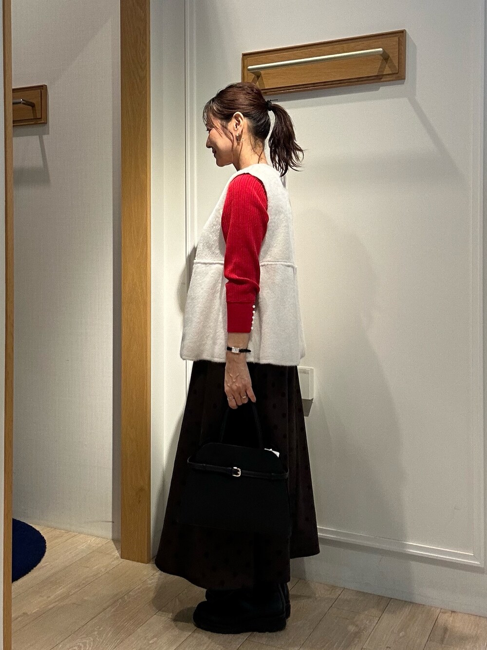 レッド系のニット/セーター、ブラウン系のスカート、ブラック系のトートバッグを着用したレディースの秋コーディネートの2枚目の写真