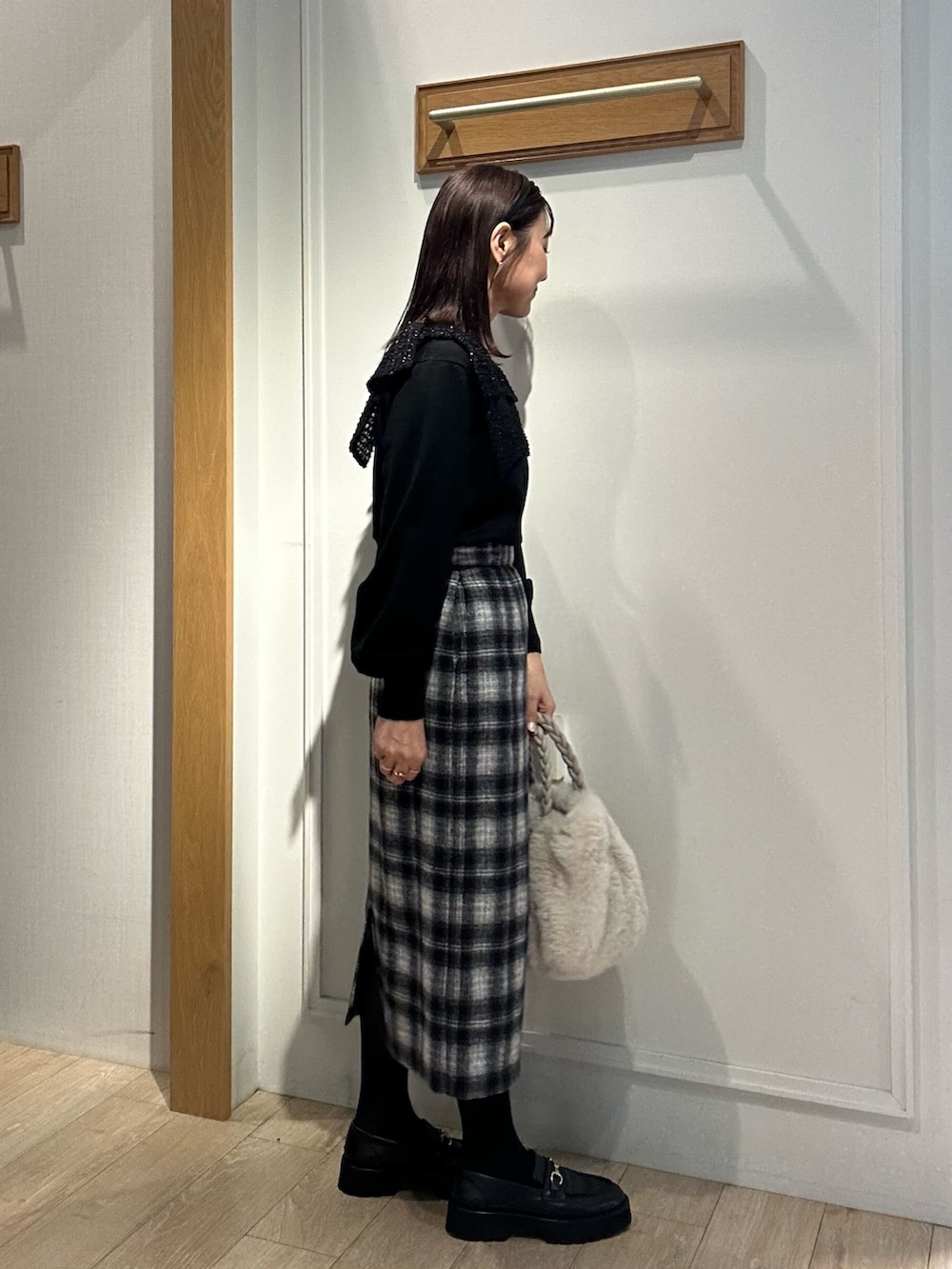 ブラック系のニット/セーター、ブルー系のスカート、ホワイト系のトートバッグを着用したレディースの冬コーディネートの2枚目の写真