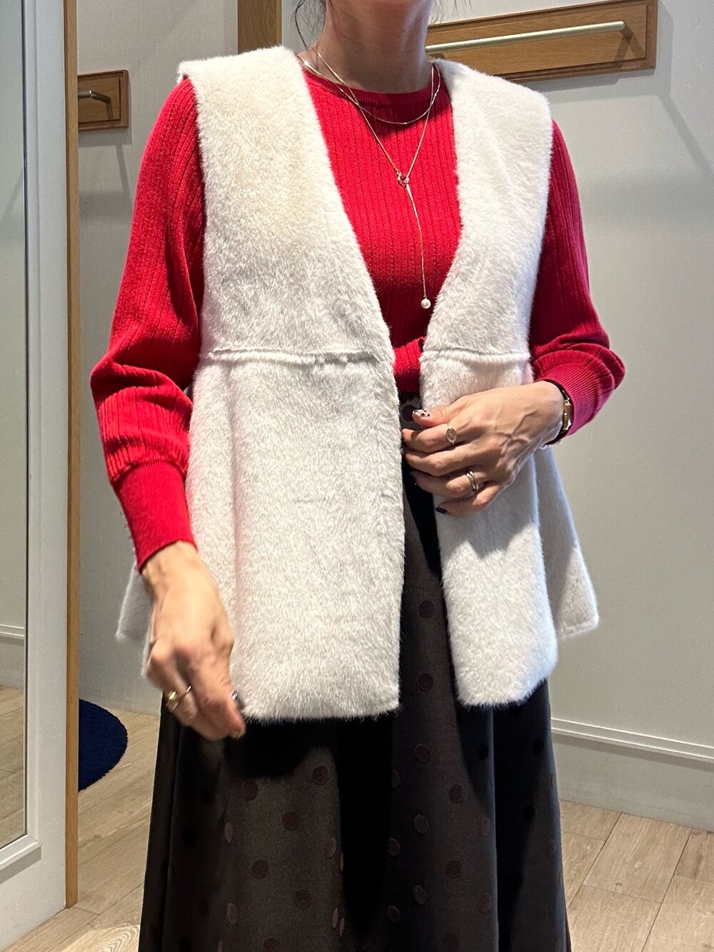 レッド系のニット/セーター、ブラウン系のスカート、ブラック系のトートバッグを着用したレディースの秋コーディネートの3枚目の写真