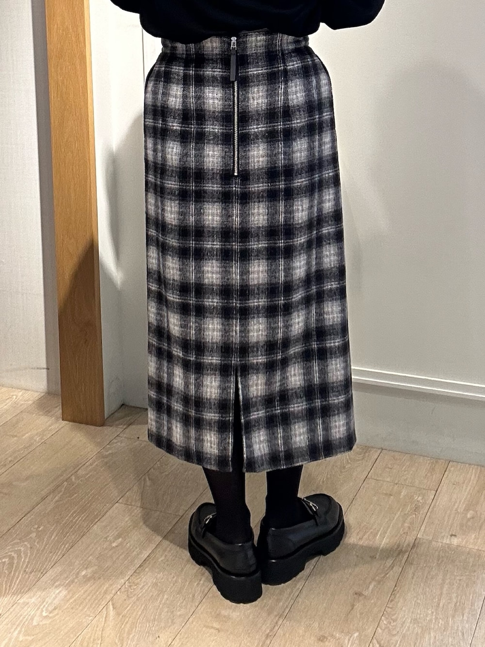 ブラック系のニット/セーター、ブルー系のスカート、ホワイト系のトートバッグを着用したレディースの冬コーディネートの9枚目の写真