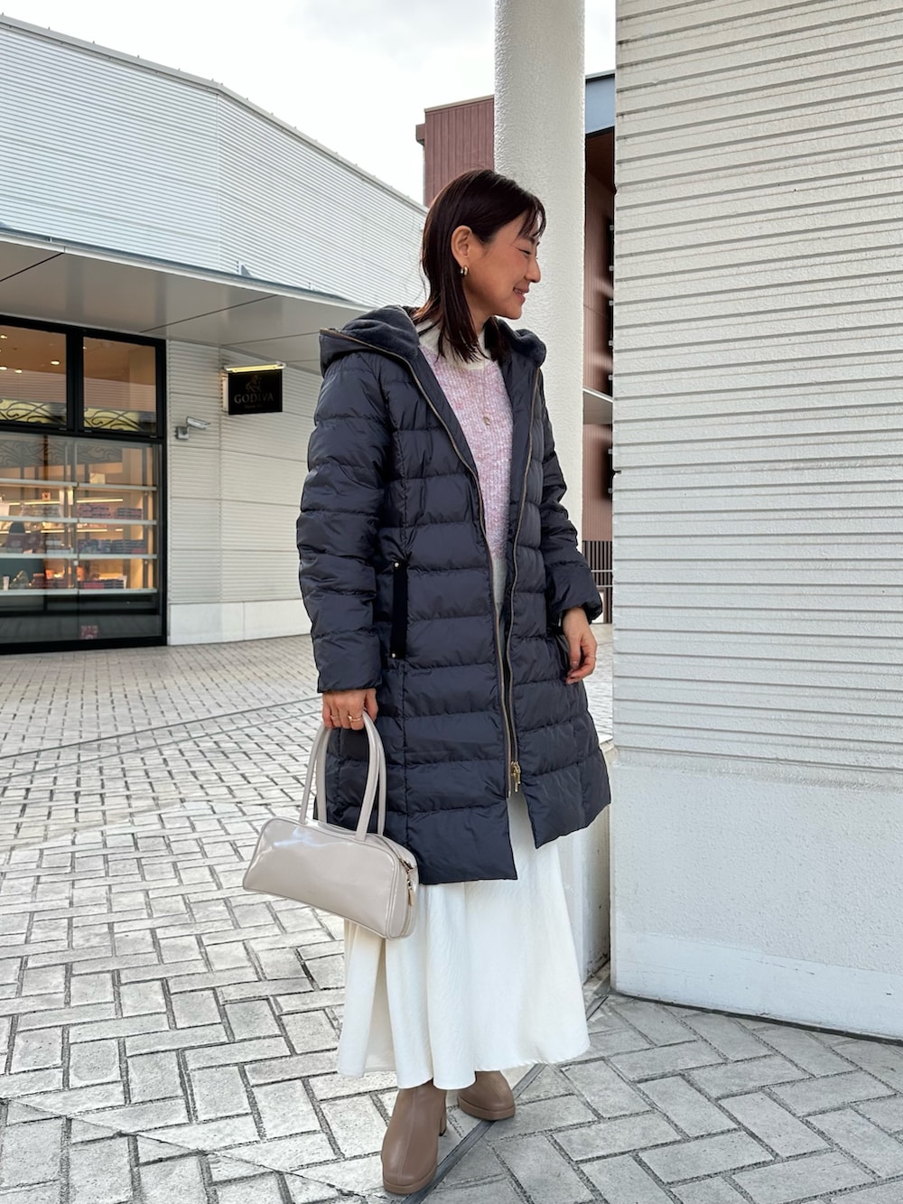 ピンク系のニット/セーター、グレー系のダウンジャケット/コート、ホワイト系のスカートを着用したレディースの冬コーディネートの2枚目の写真