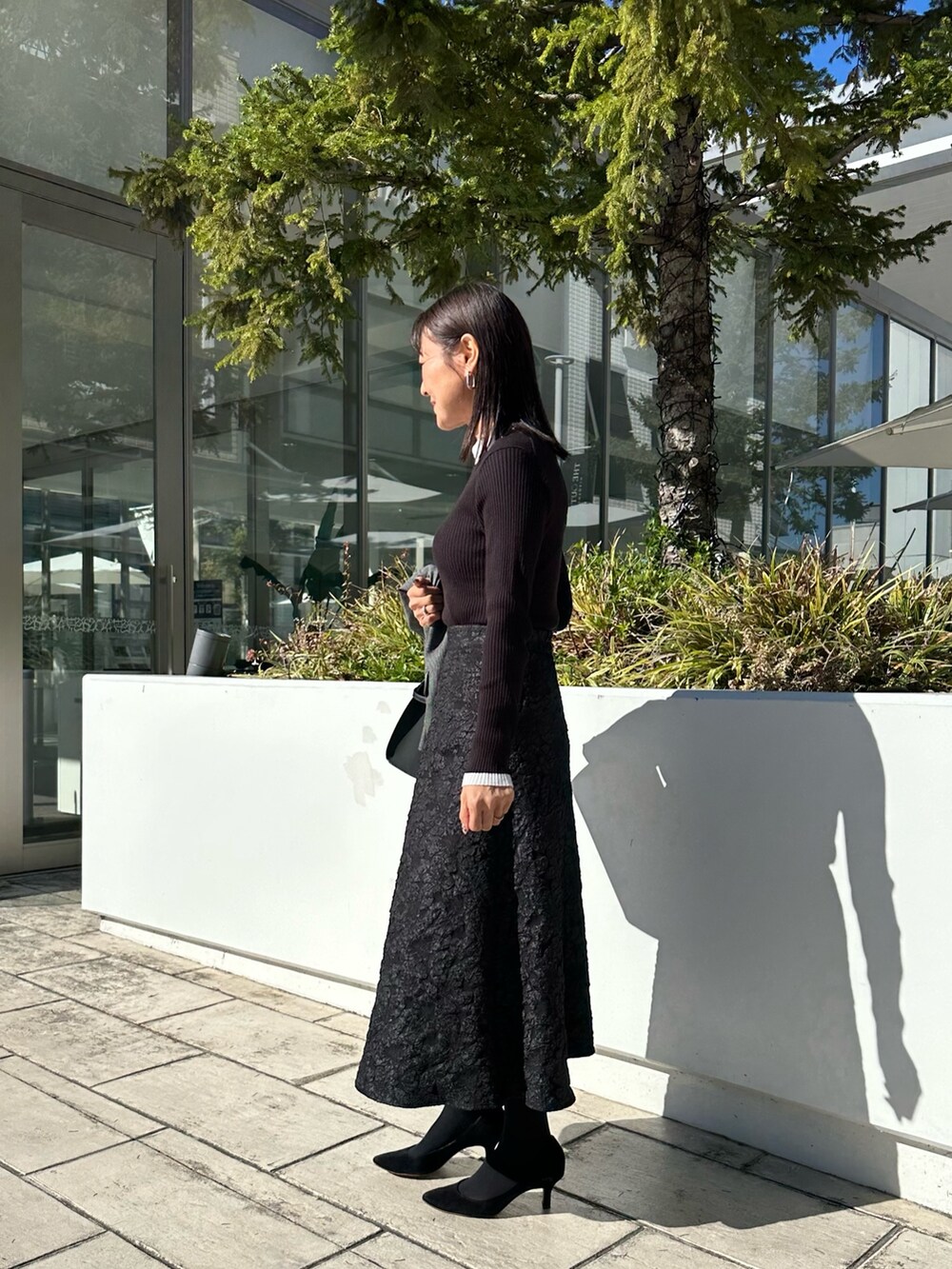 グレー系のテーラードジャケット、ブラック系のニット/セーター、グレー系のスカートを着用したレディースの秋コーディネートの9枚目の写真