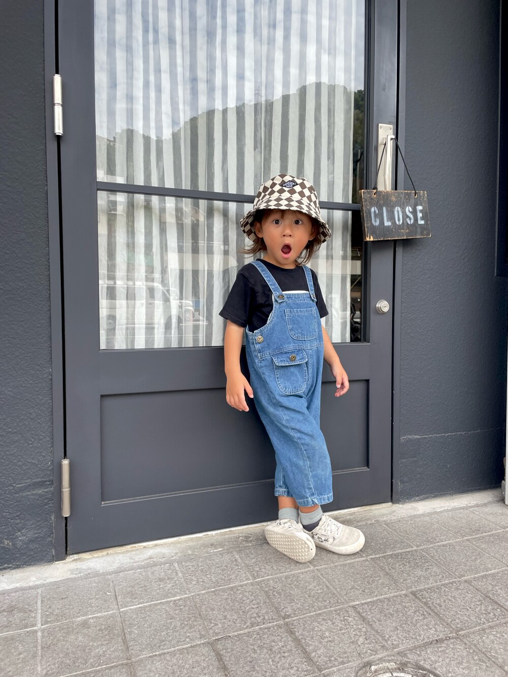 ホワイト系のスニーカー、ブルー系のオールインワン・サロペット、ブラック系のショルダーバッグを着用したキッズの秋コーディネートの2枚目の写真