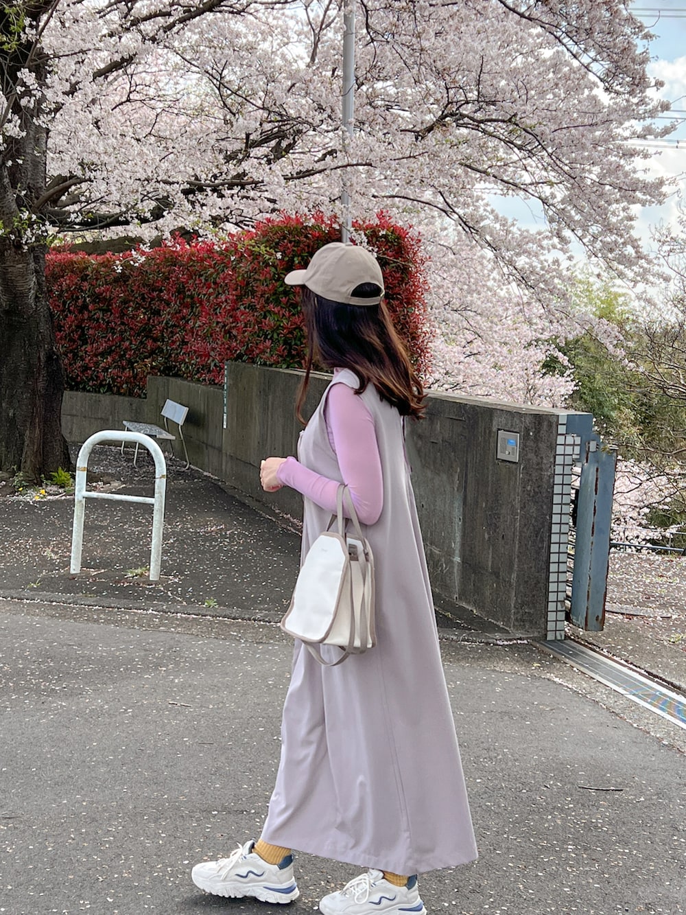 パープル系のTシャツ/カットソー、グレー系のジャンパースカート、ベージュ系のキャップを着用したレディースの春コーディネートの2枚目の写真