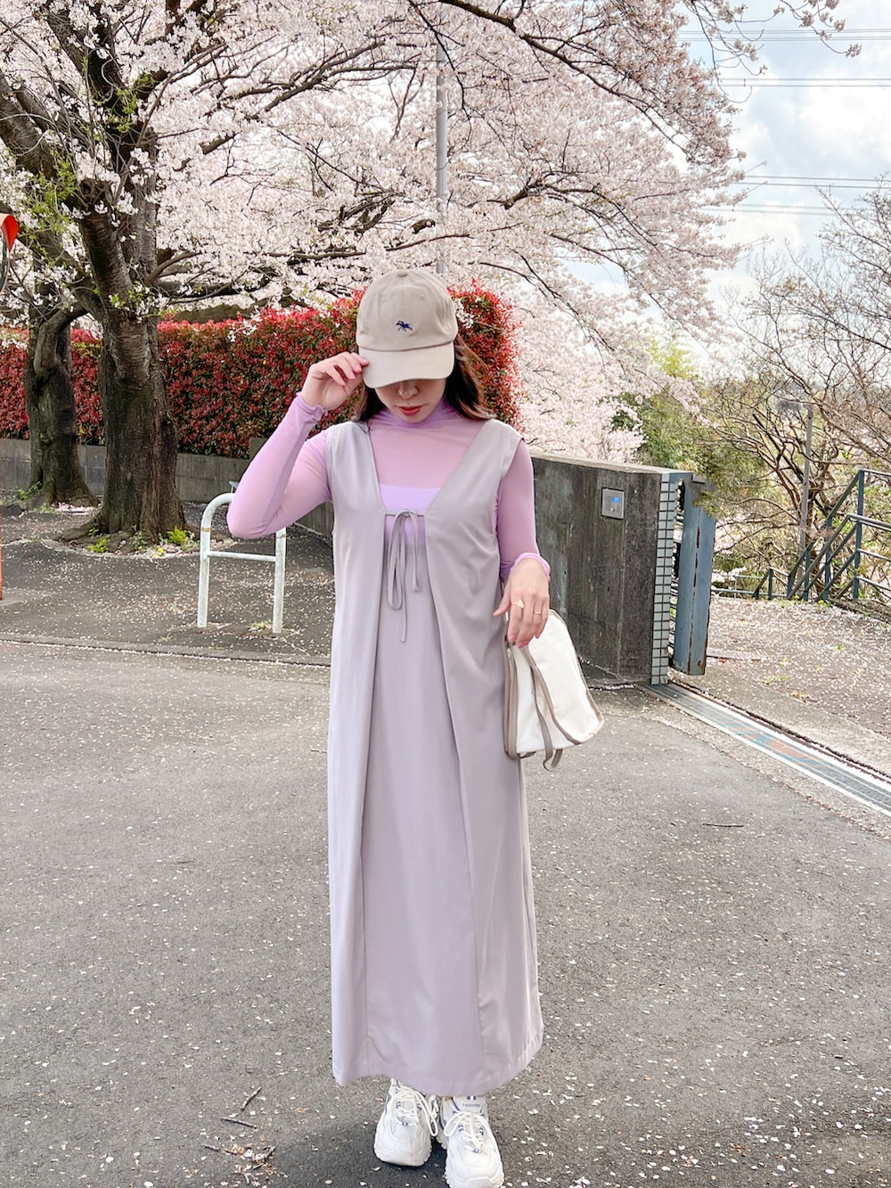 パープル系のTシャツ/カットソー、グレー系のジャンパースカート、ベージュ系のキャップを着用したレディースの春コーディネートの3枚目の写真