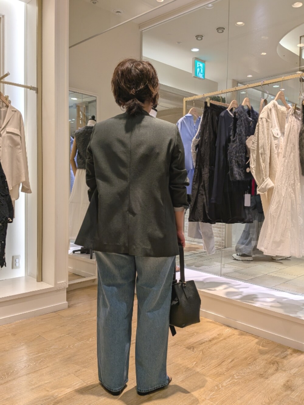 グレー系のノーカラージャケット、ブルー系のデニムパンツ、ブラック系のショルダーバッグを着用したレディースの秋コーディネートの4枚目の写真