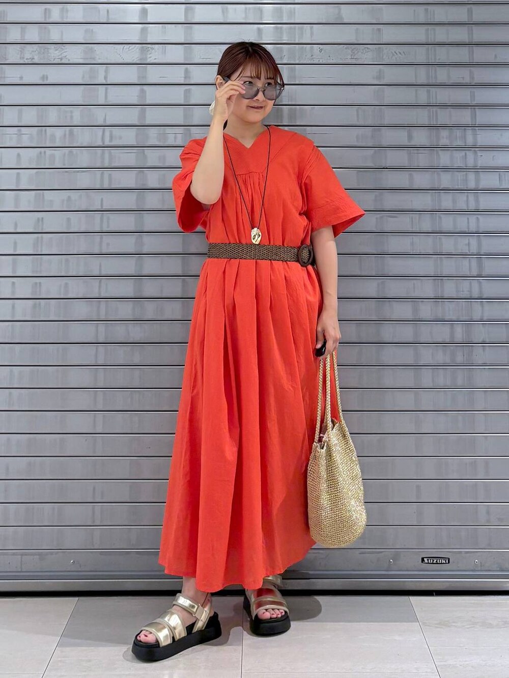 オレンジ系のワンピース、ゴールド系のサンダル、ゴールド系のトートバッグを着用したレディースの夏コーディネートの2枚目の写真