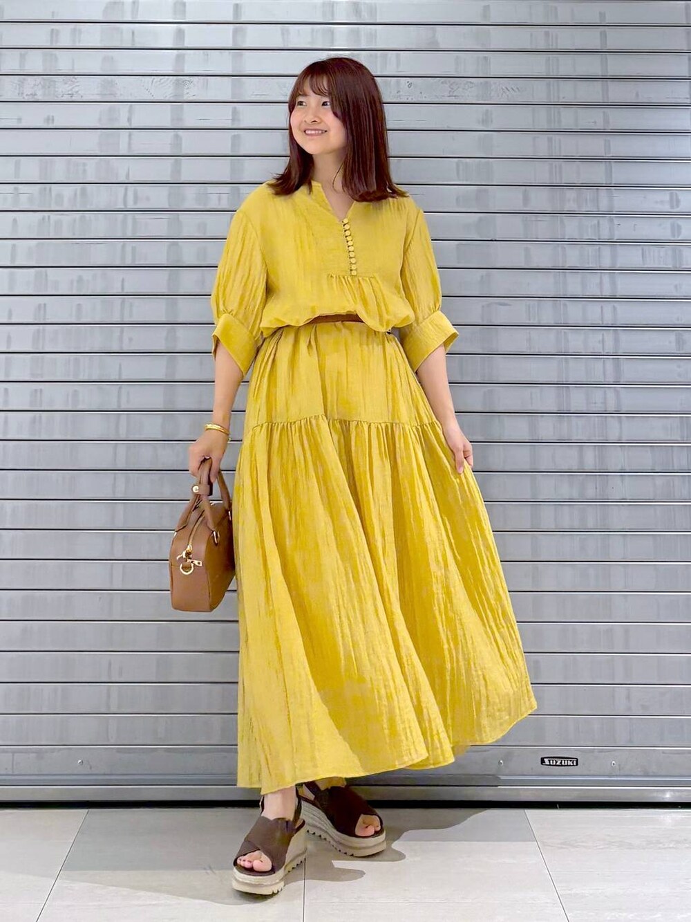 ブラウン系のハンドバッグ、イエロー系のワンピース、ブラウン系のベルトを着用したレディースの夏コーディネートの2枚目の写真