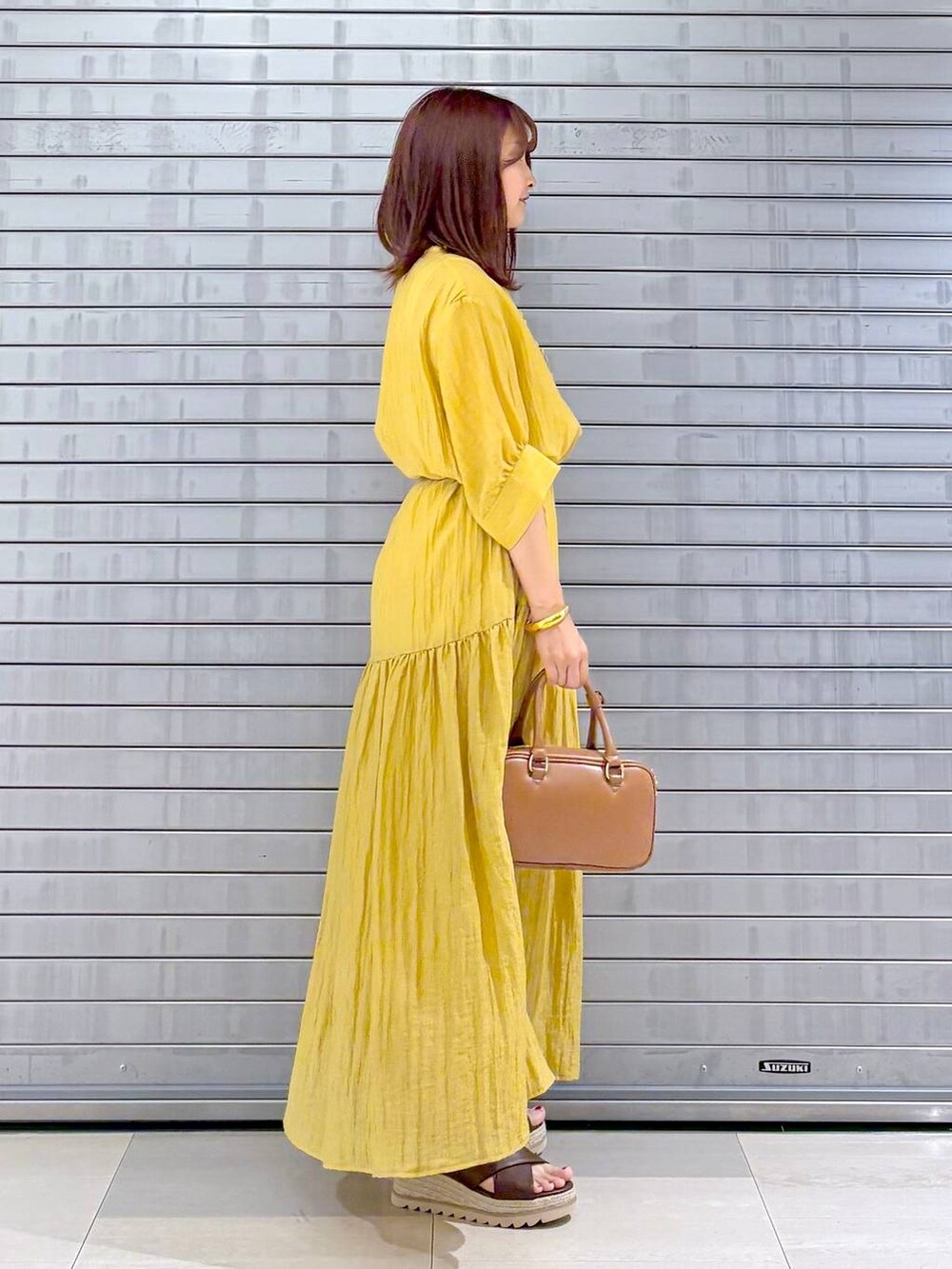 ブラウン系のハンドバッグ、イエロー系のワンピース、ブラウン系のベルトを着用したレディースの夏コーディネートの3枚目の写真