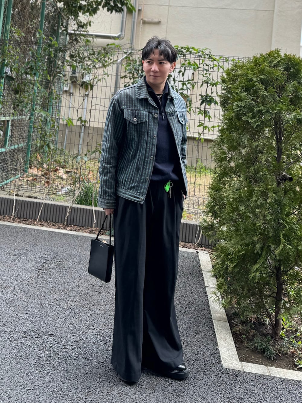 パープル系のトップス、グリーン系のデニムジャケット、ブラック系のショルダーバッグを着用したメンズの春コーディネートの4枚目の写真