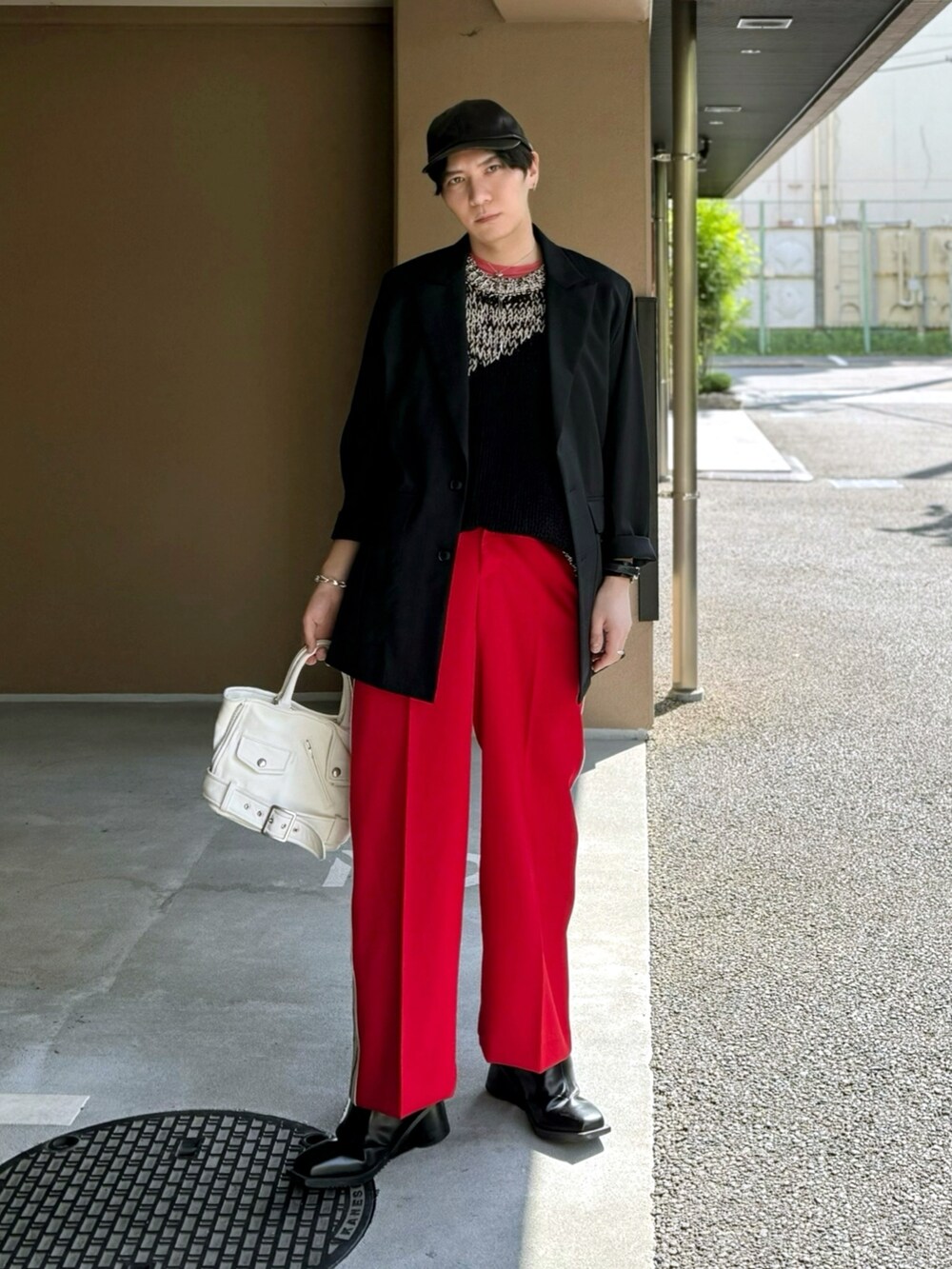 レッド系のスラックス、ホワイト系のハンドバッグ、ブラック系のブーツを着用したメンズの春コーディネートの3枚目の写真