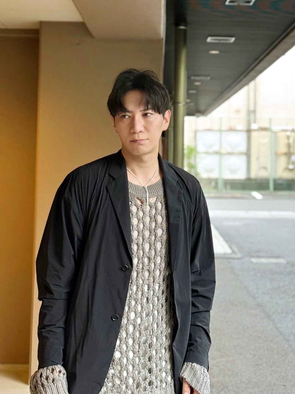 グレー系のニット/セーター、ブラック系のテーラードジャケット、ブラウン系のショルダーバッグを着用したメンズの秋コーディネートの3枚目の写真