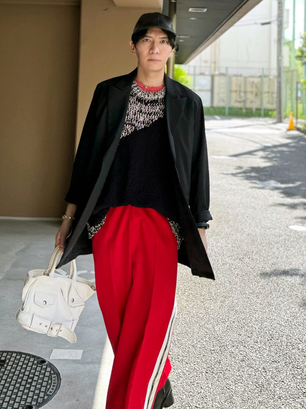 レッド系のスラックス、ホワイト系のハンドバッグ、ブラック系のブーツを着用したメンズの春コーディネートの4枚目の写真