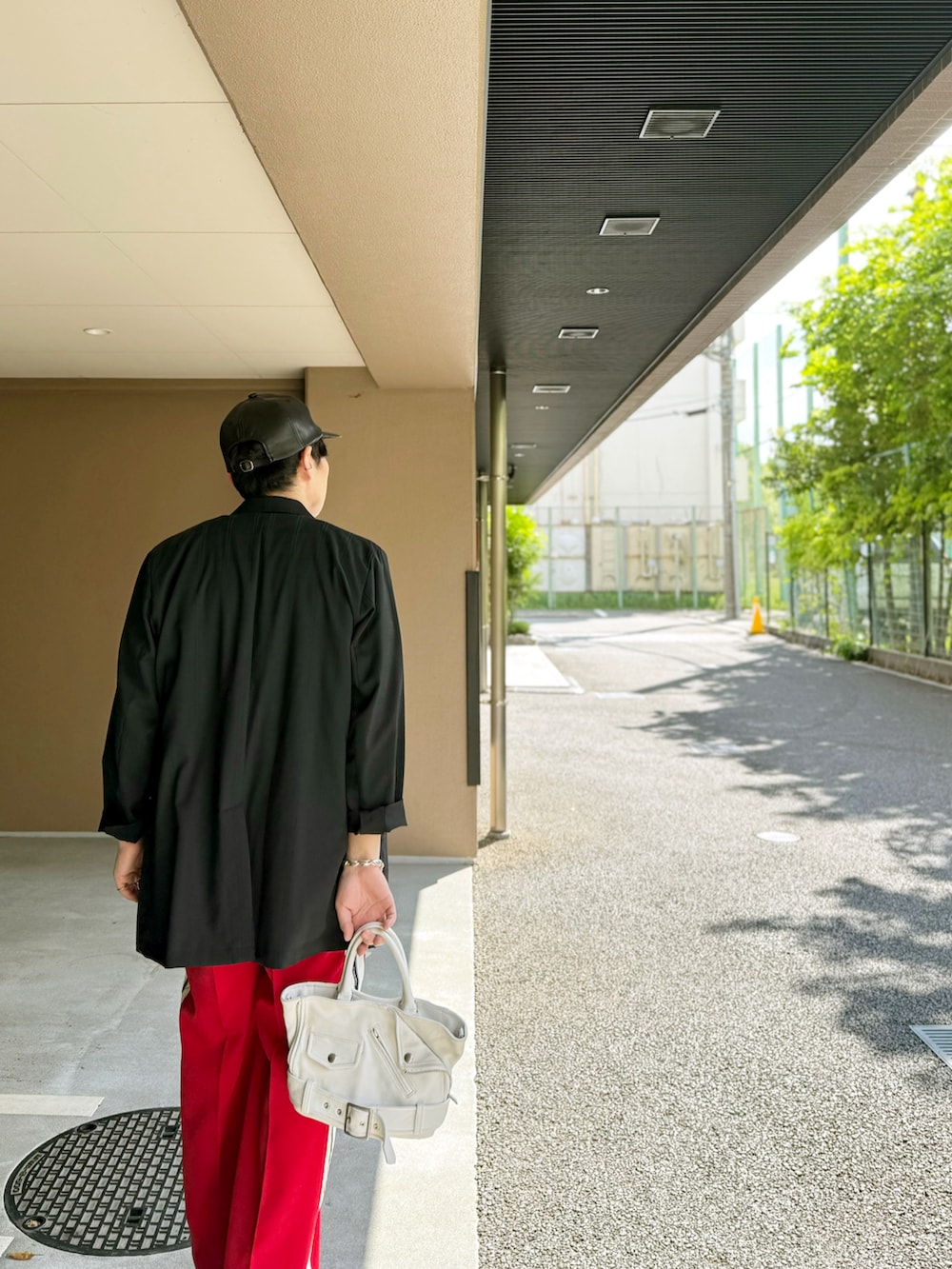 レッド系のスラックス、ホワイト系のハンドバッグ、ブラック系のブーツを着用したメンズの春コーディネートの2枚目の写真