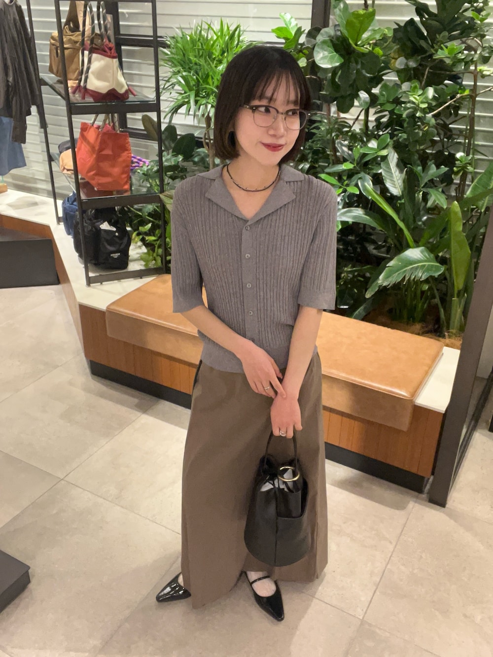 グレー系のニット/セーター、グレー系のスカート、ブラック系のハンドバッグを着用したレディースの春コーディネートの2枚目の写真