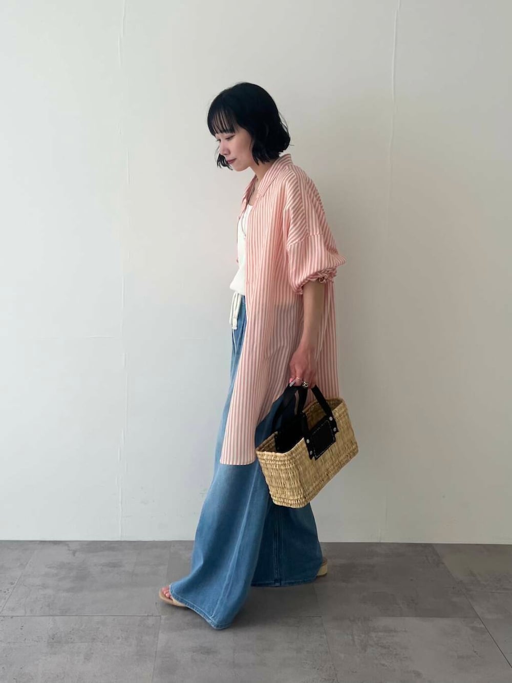 ブラック系のかごバッグ、ブルー系のデニムパンツ、ホワイト系のベストを着用したレディースの春コーディネートの4枚目の写真