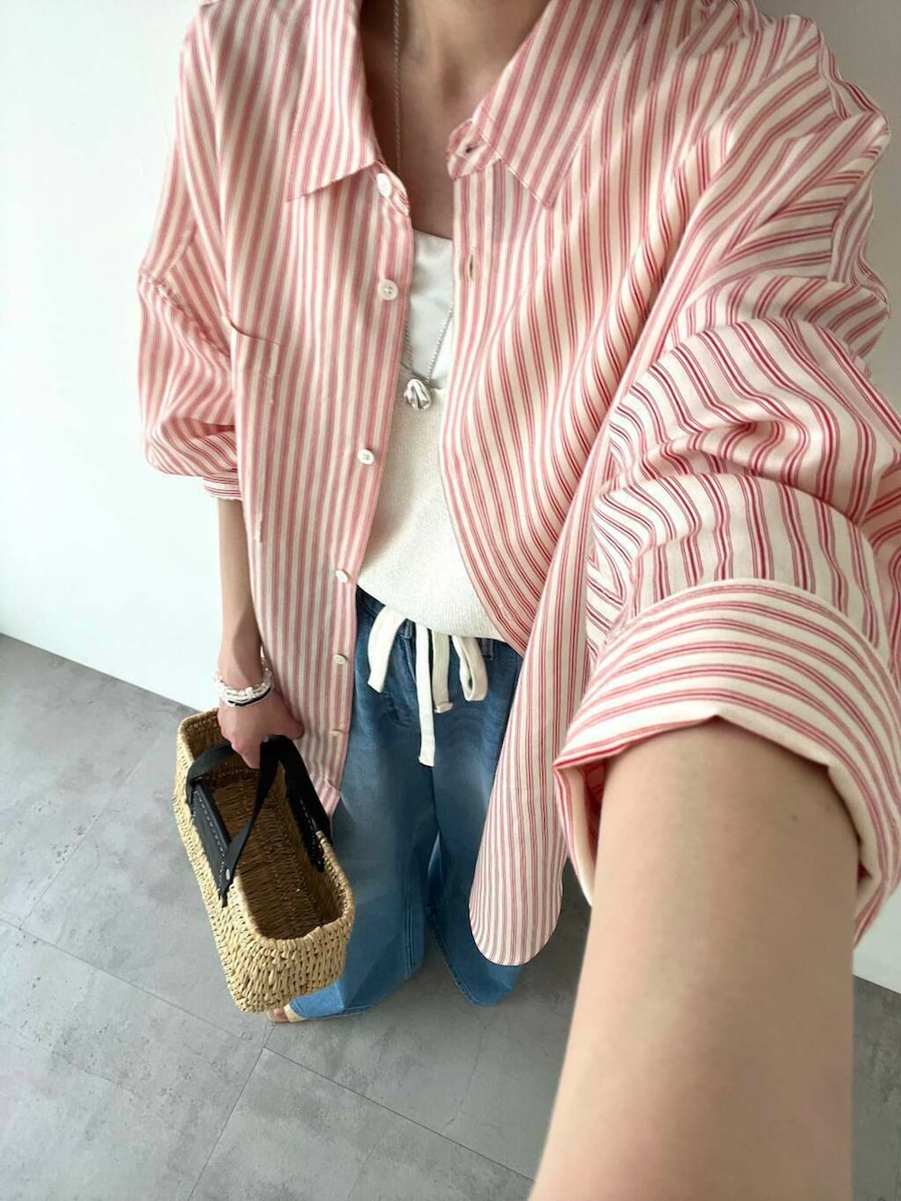 ブラック系のかごバッグ、ブルー系のデニムパンツ、ホワイト系のベストを着用したレディースの春コーディネートの7枚目の写真