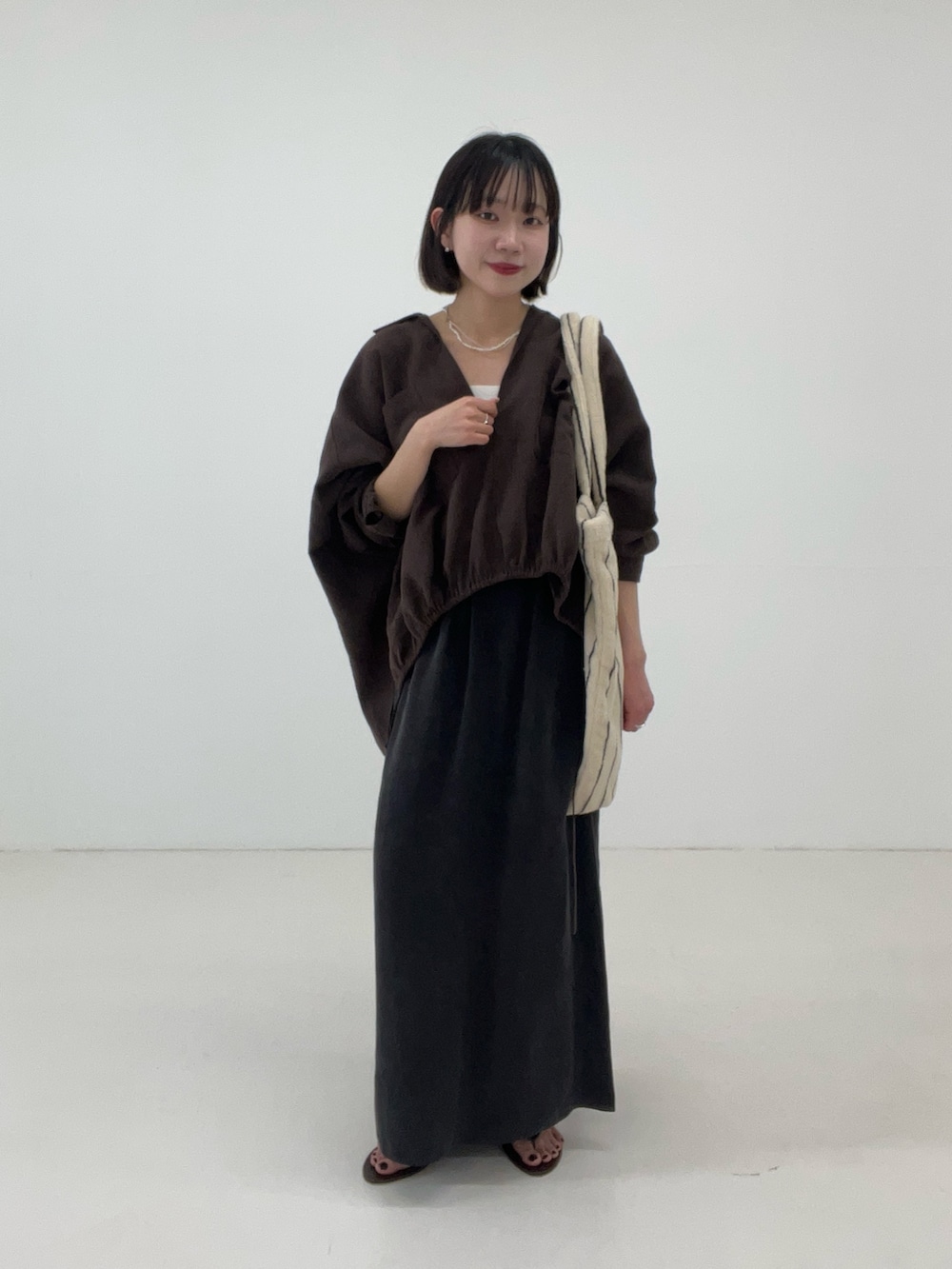 ブラウン系のシャツ/ブラウス、グレー系のスカート、ホワイト系のトートバッグを着用したレディースの春コーディネートの2枚目の写真