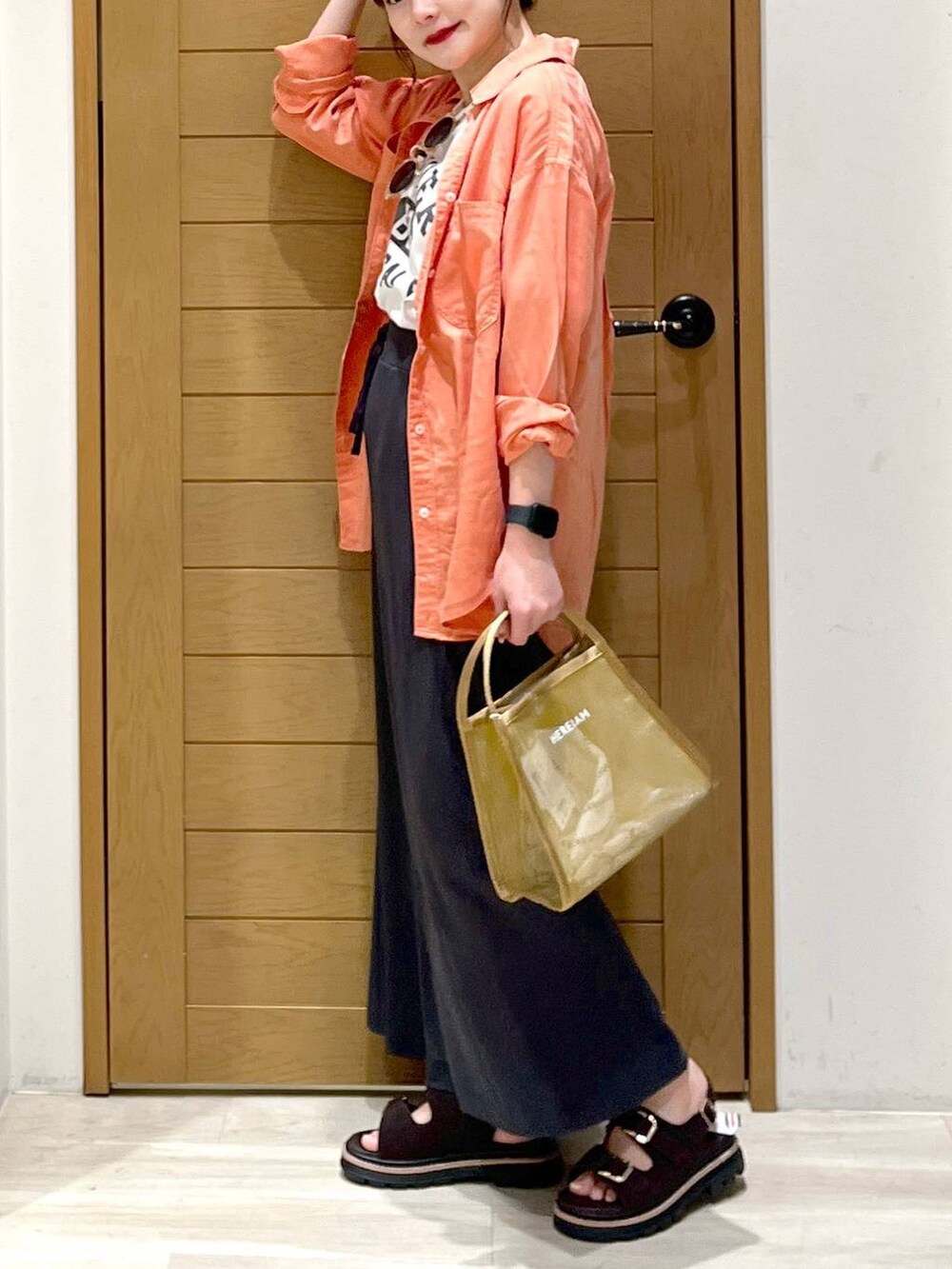 オレンジ系のシャツ/ブラウス、ブラウン系のサンダル、ホワイト系のTシャツ/カットソーを着用したレディースの春コーディネートの2枚目の写真