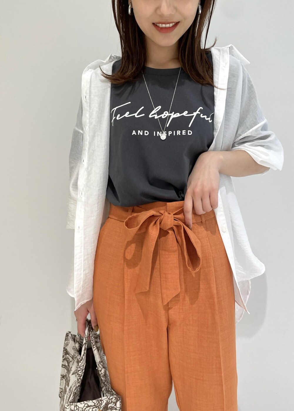 ブラウン系のトートバッグ、オレンジ系のスラックス、ブラック系のTシャツ/カットソーを着用したレディースの春コーディネートの3枚目の写真