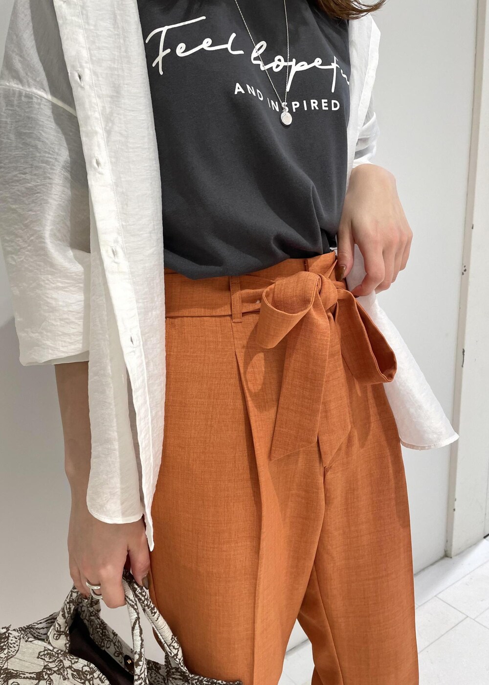 ブラウン系のトートバッグ、オレンジ系のスラックス、ブラック系のTシャツ/カットソーを着用したレディースの春コーディネートの4枚目の写真