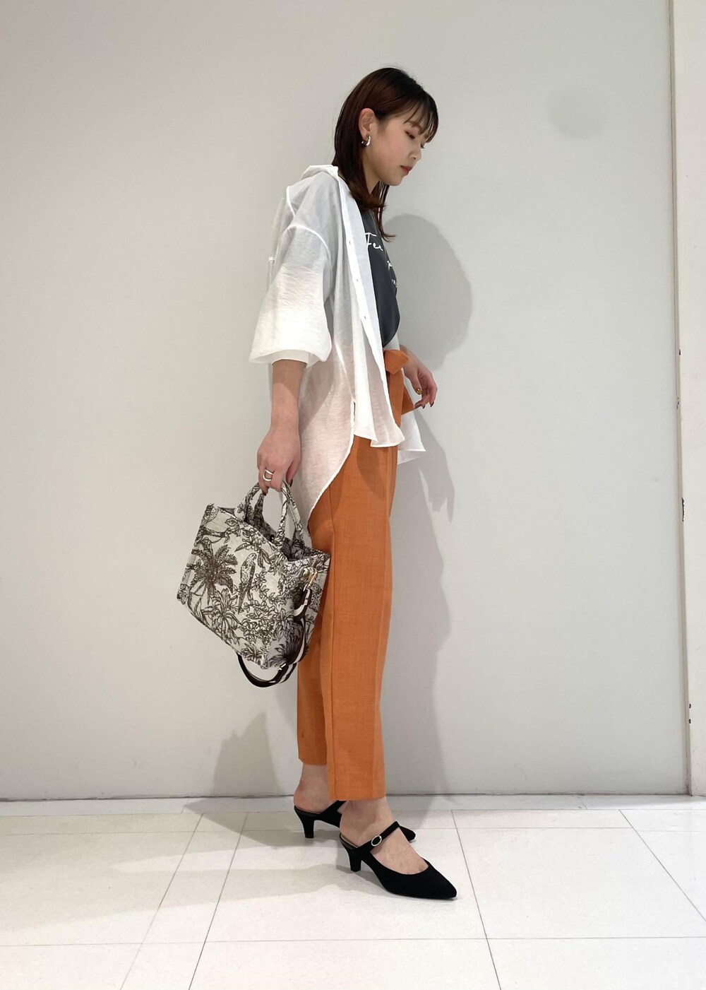 ブラウン系のトートバッグ、オレンジ系のスラックス、ブラック系のTシャツ/カットソーを着用したレディースの春コーディネートの2枚目の写真