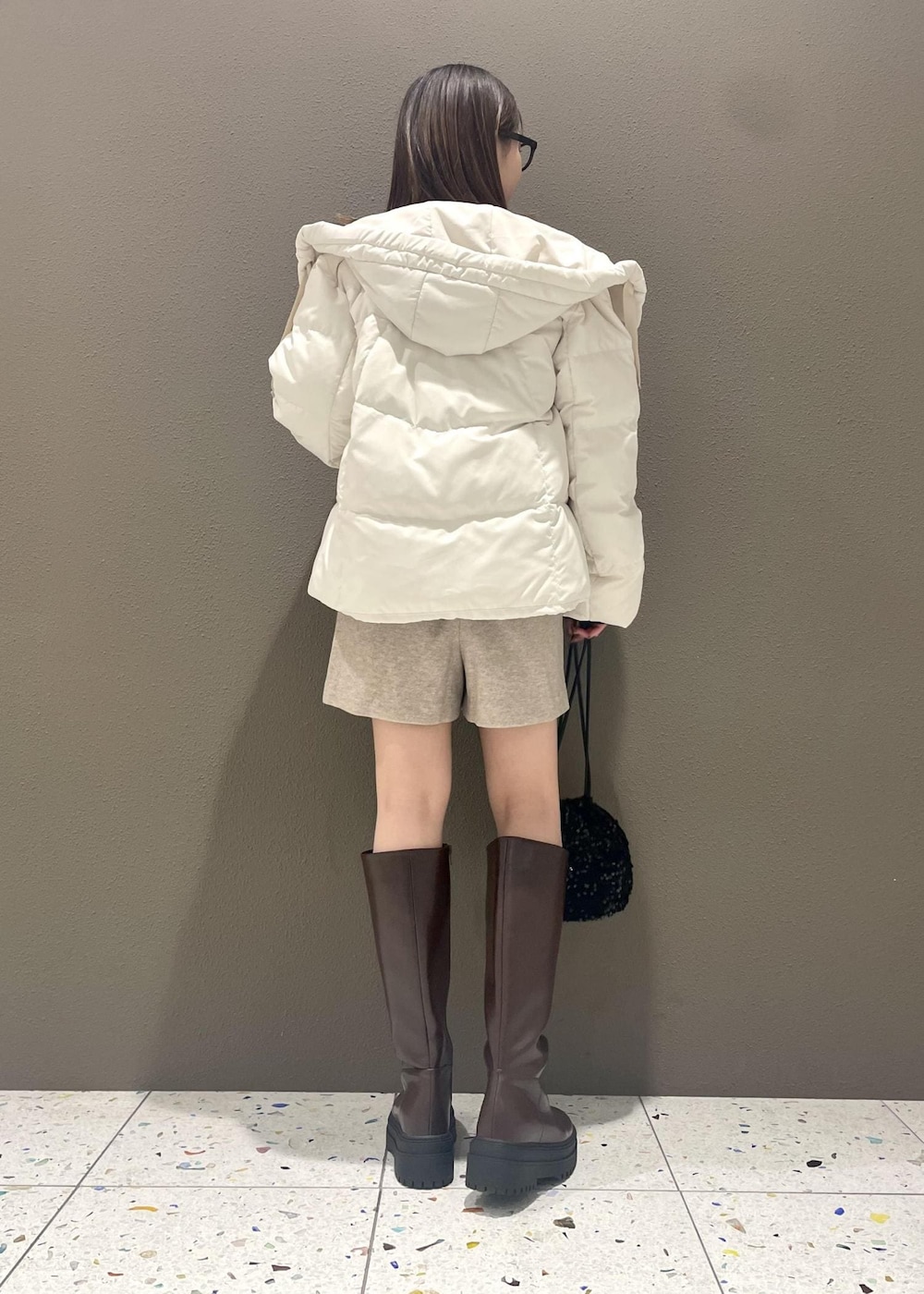 ブラウン系のブーツ、ホワイト系のダウンジャケット/コート、グレー系のニット/セーターを着用したレディースの冬コーディネートの2枚目の写真