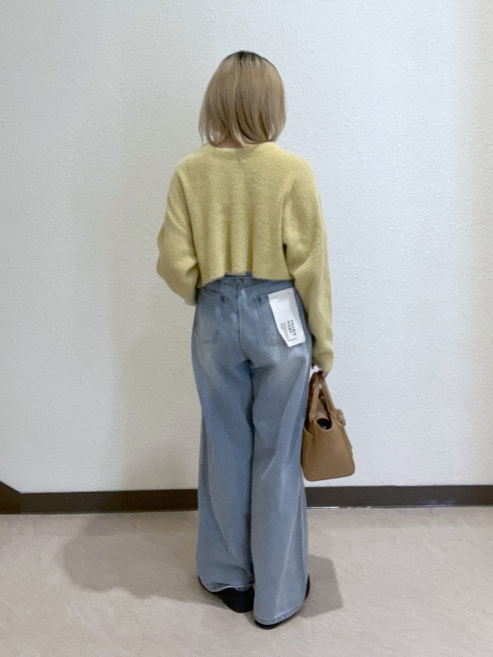 イエロー系のニット/セーター、ブルー系のデニムパンツ、ベージュ系のトートバッグを着用したレディースの秋コーディネートの3枚目の写真